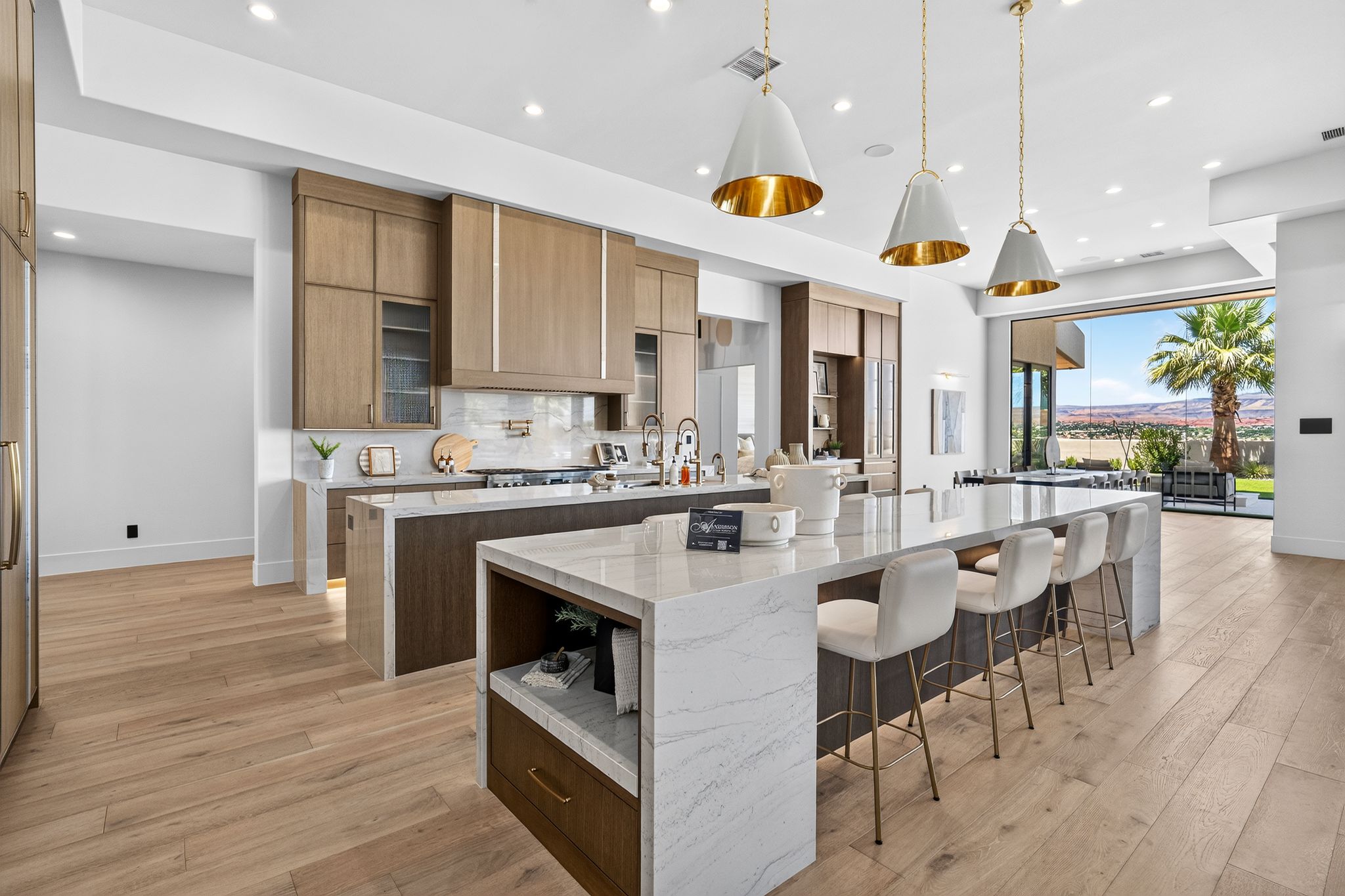 Gourmet kitchen featuring a large central island with seating, wood-finish flooring, custom cabinetry, recessed lighting, and expansive sliding glass doors opening to outdoor scenery