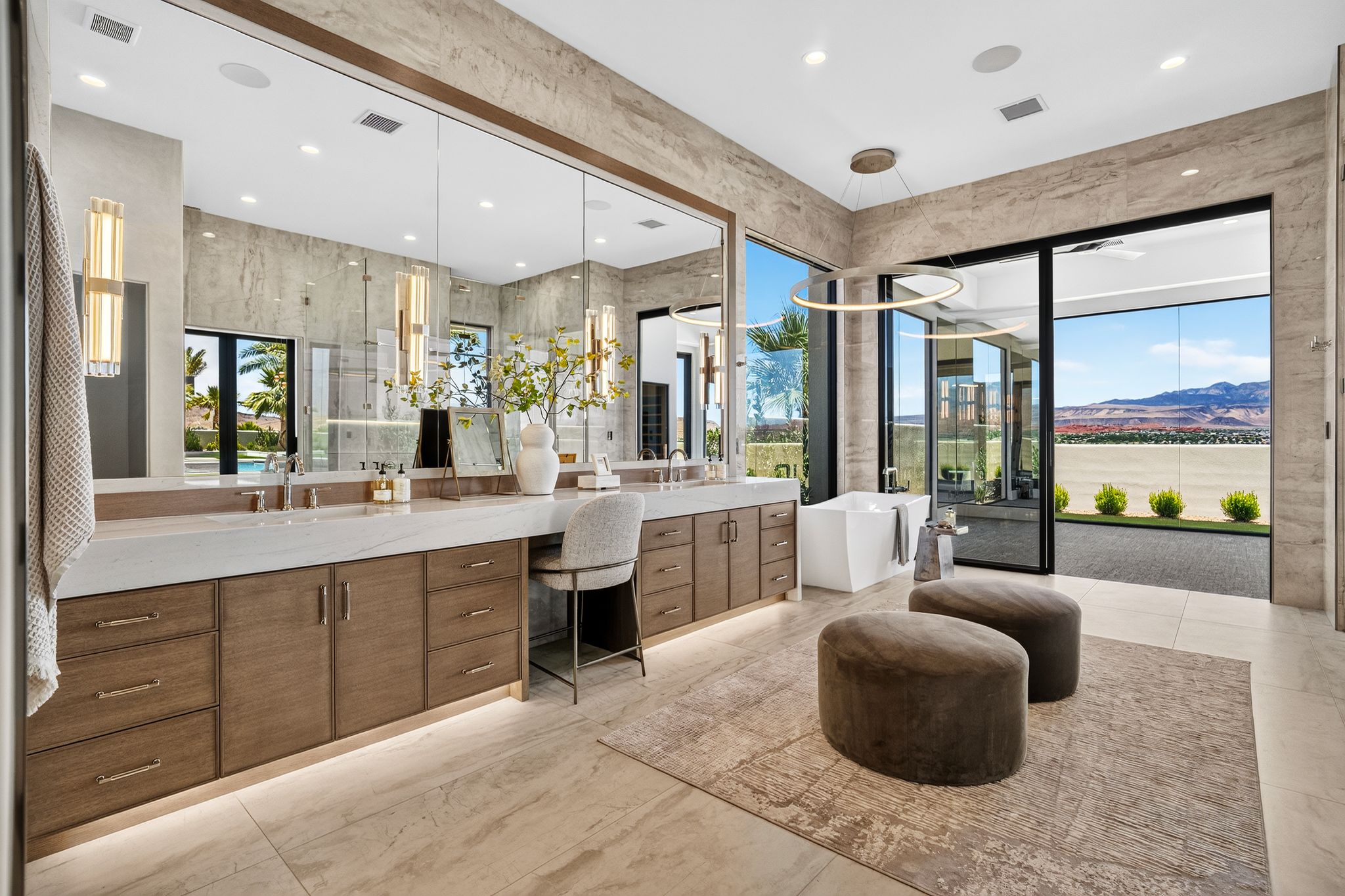 Spacious bathroom featuring a freestanding tub, expansive vanity with dual sinks, large format tile flooring, a full-wall mirror, and sliding glass doors opening to an outdoor patio with mountain scenery