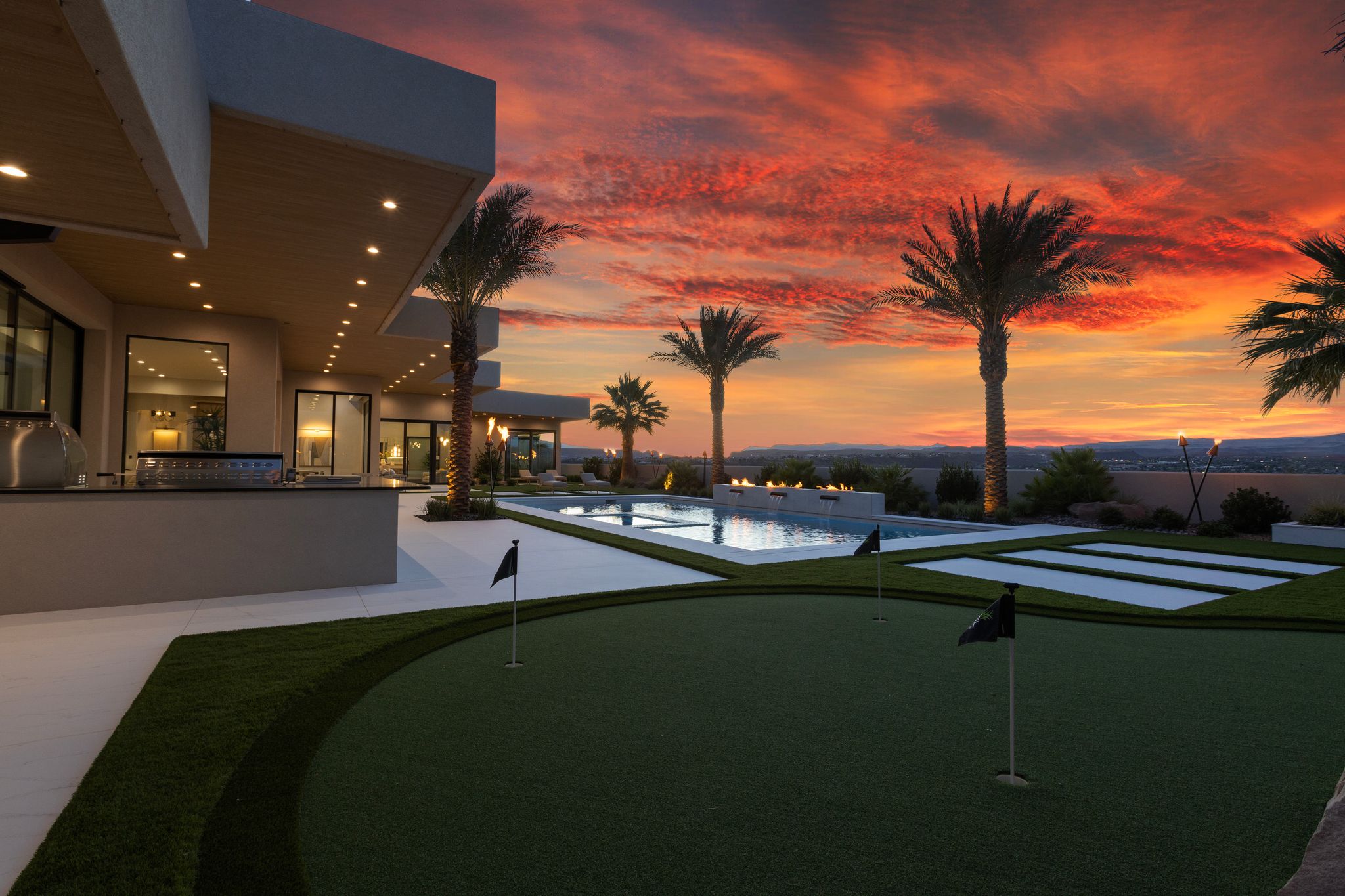 Outdoor putting green, expansive patio, integrated outdoor kitchen with built-in grill, rectangular pool, and mature palm trees