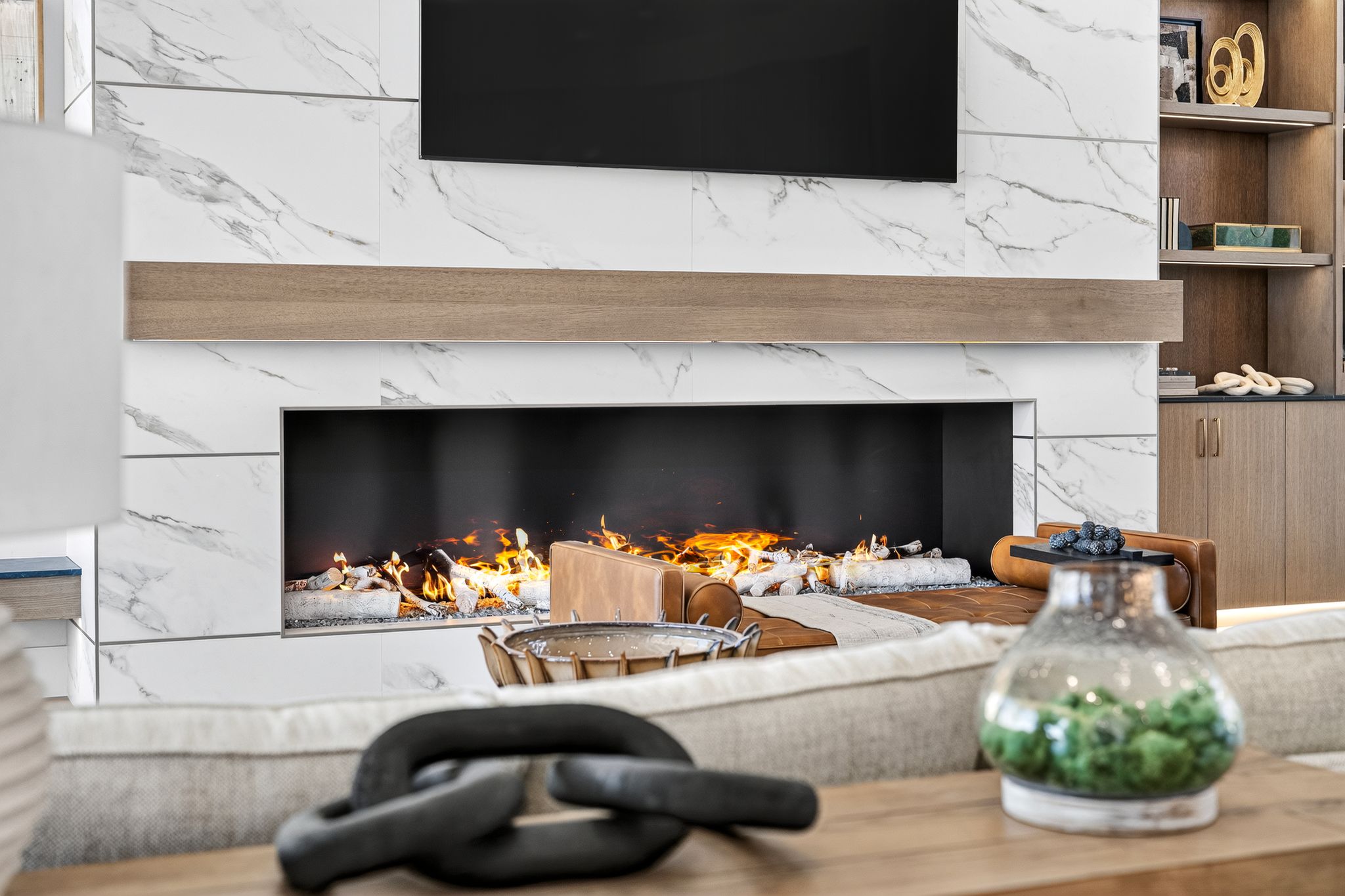 Modern linear fireplace featuring a white marble-look surround, a wood-finish mantel, and an integrated media wall