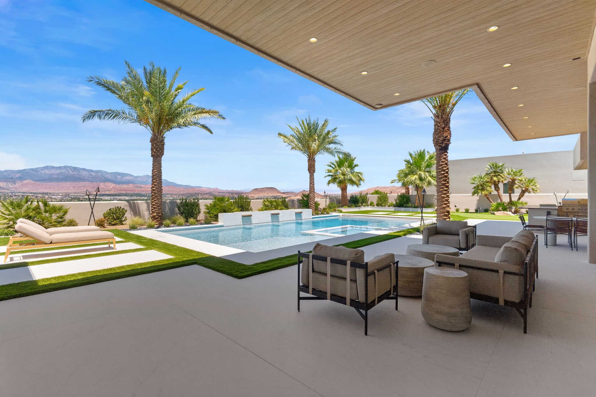 Expansive patio featuring a large swimming pool with water features, a built-in outdoor kitchen, and concrete hardscaping