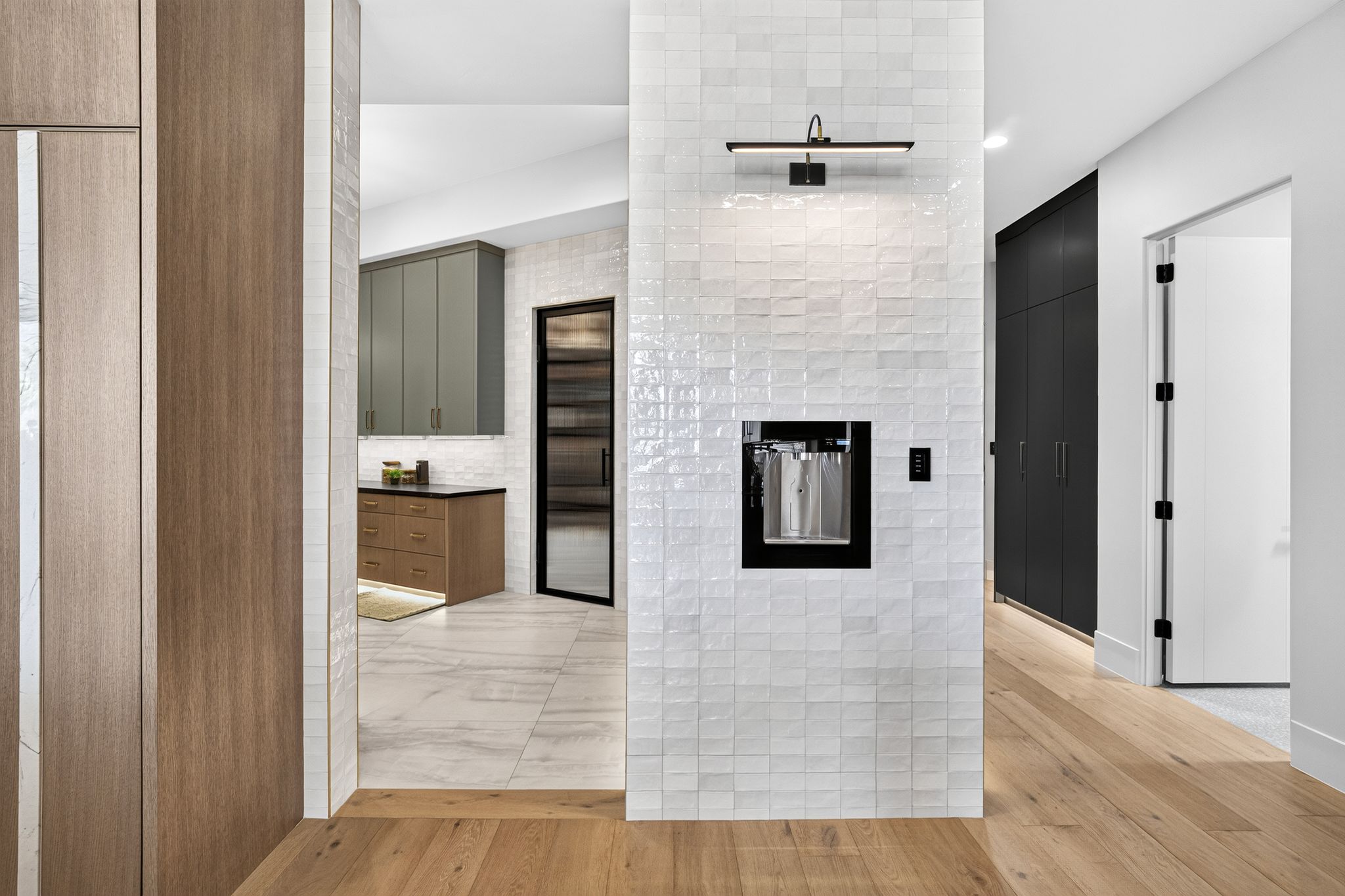Integrated beverage station set within textured white tile, featuring a modern wall sconce