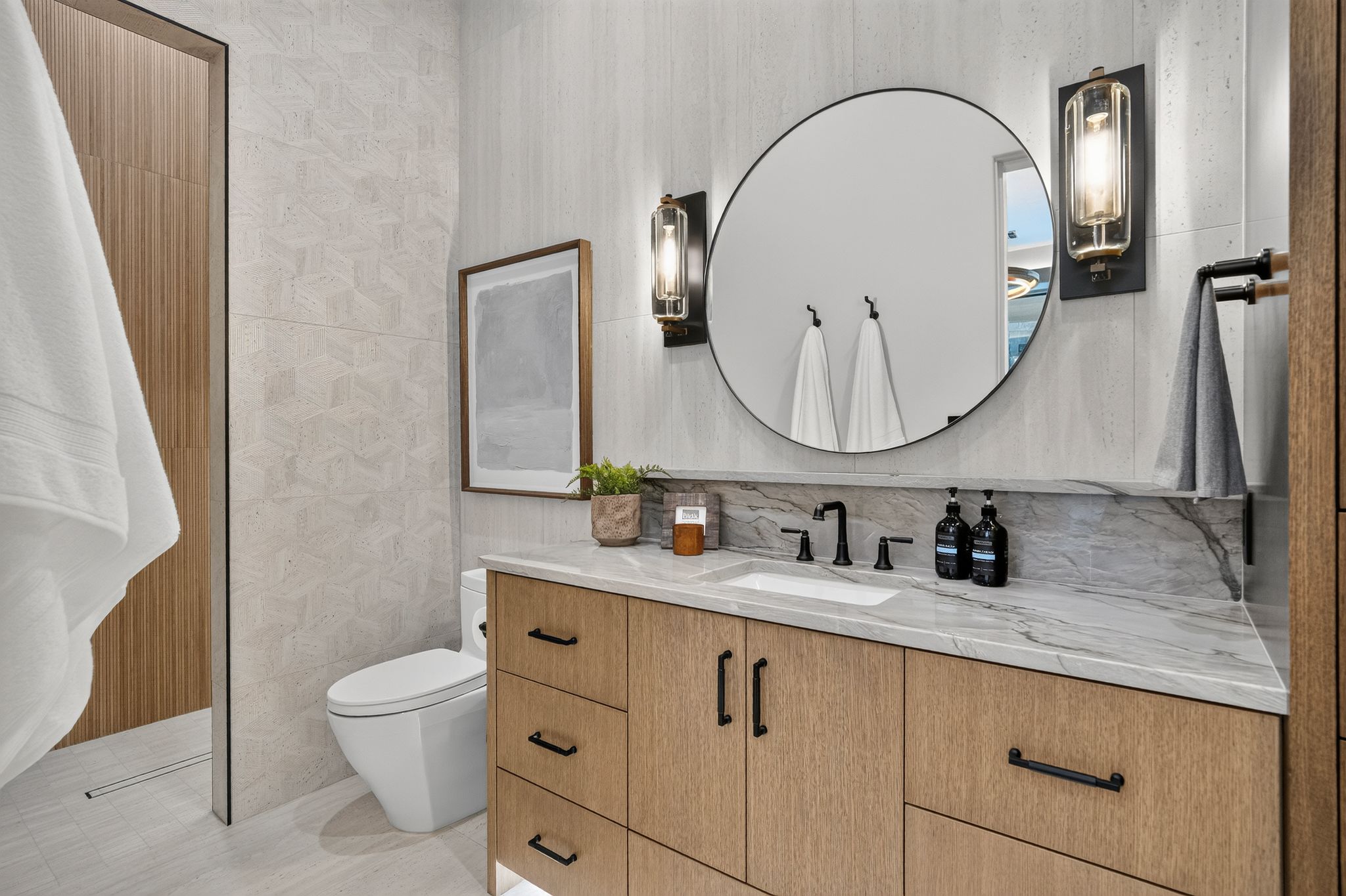 Bathroom vanity featuring a light wood-finish cabinet with black hardware, a rectangular undermount sink, and a marbled countertop with a matching backsplash