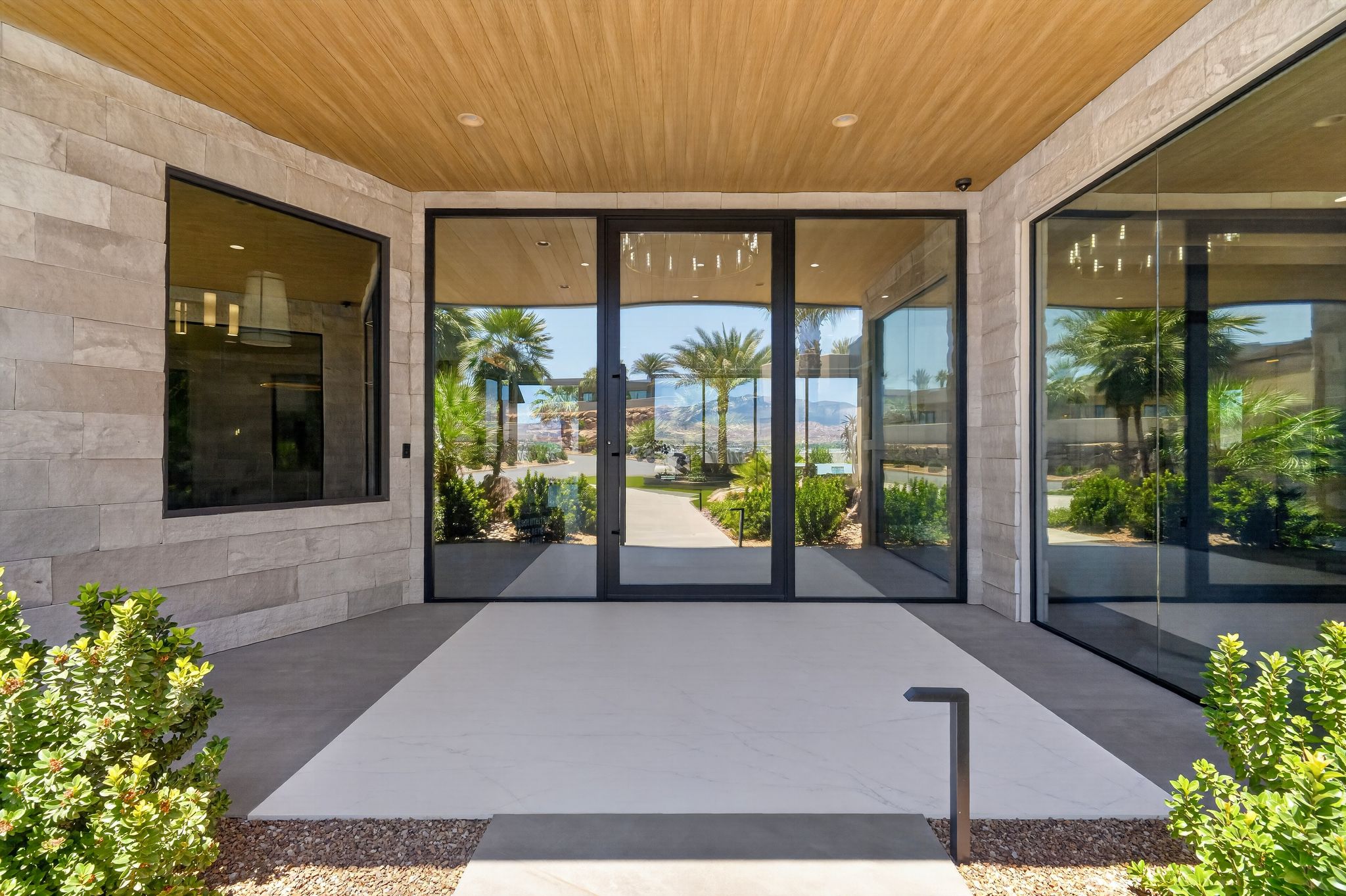 Modern entryway with a wood-finish ceiling, stone veneer exterior, and large black-framed glass doors