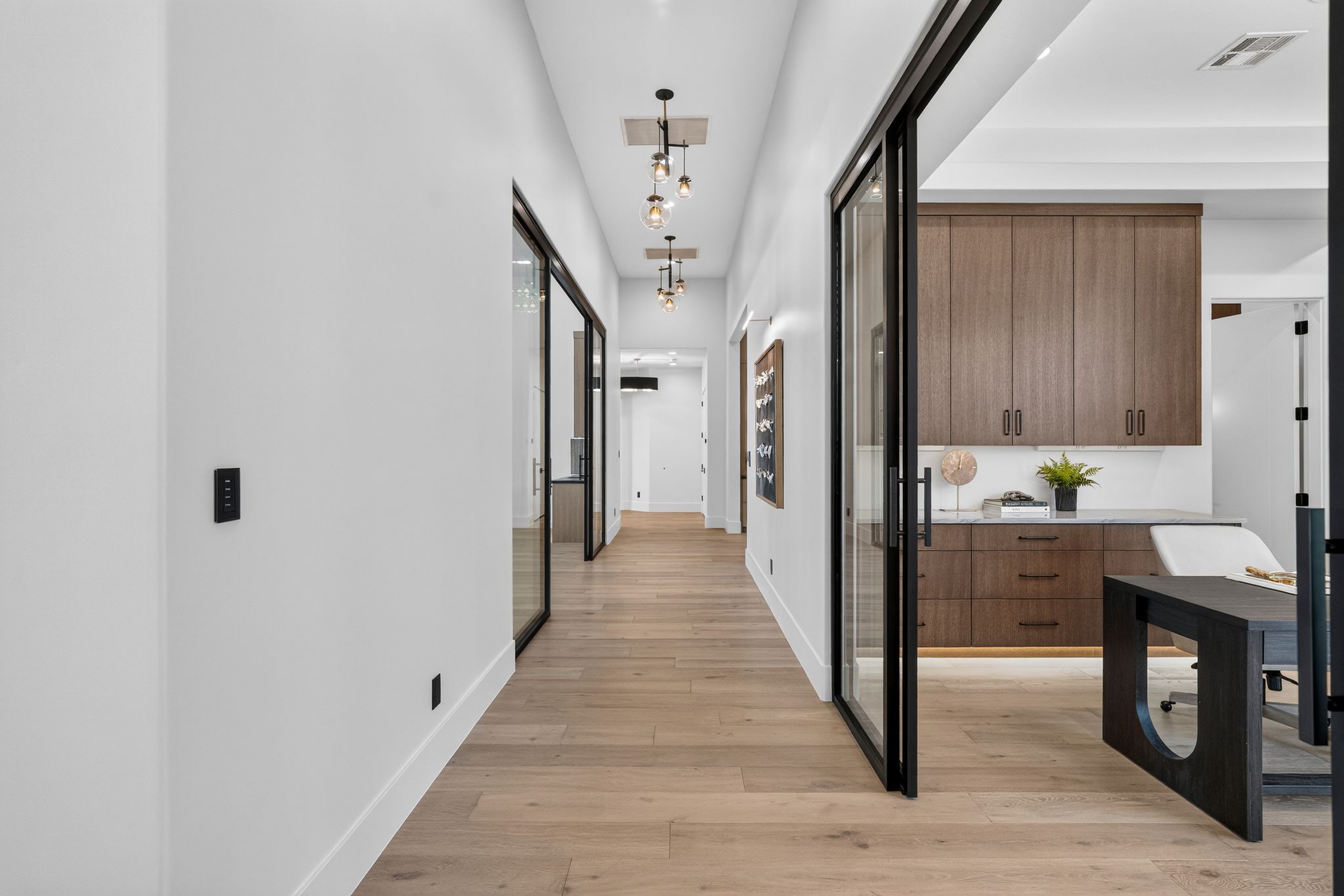 Bright hallway featuring light wood-finish flooring and contemporary pendant lighting