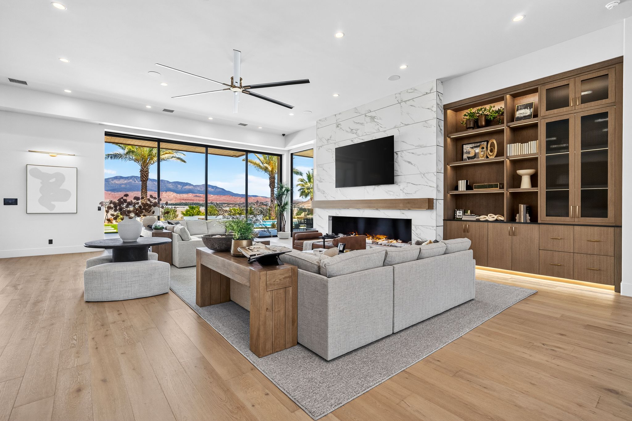 Spacious living area featuring expansive floor-to-ceiling windows, a modern linear fireplace with a stone surround, wood-finish flooring, recessed lighting, and custom built-in cabinetry with integrated lighting