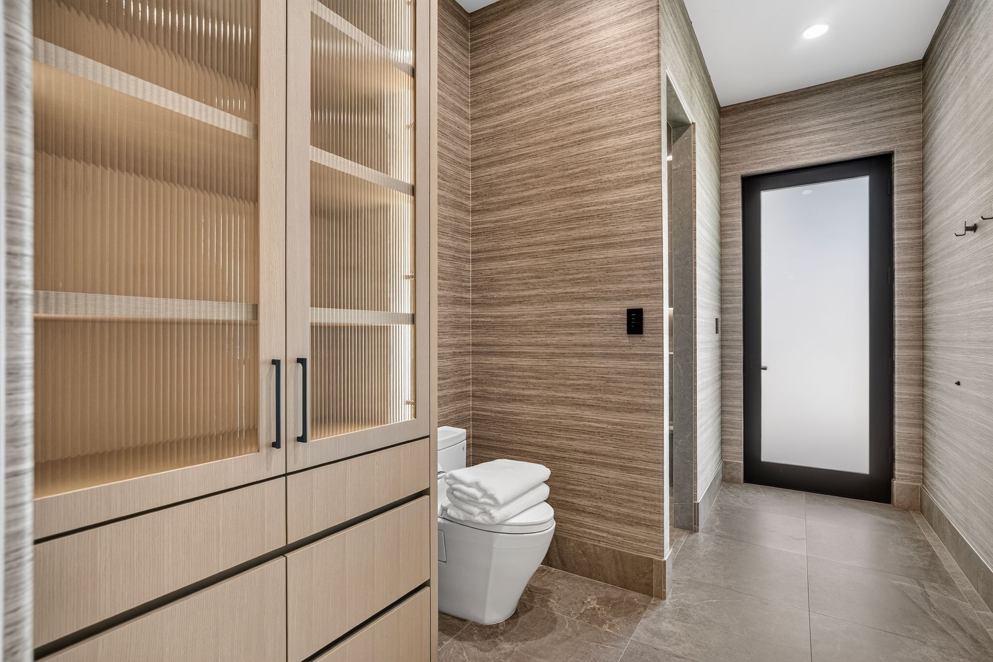 Integrated light wood-finish cabinetry featuring fluted glass panels and matte black hardware