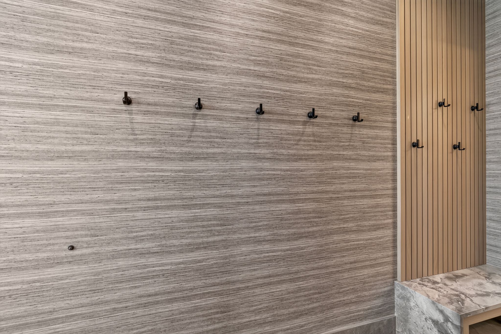 Textured wall paneling featuring integrated matte black hooks, a vertical slatted accent wall, and a built-in stone bench