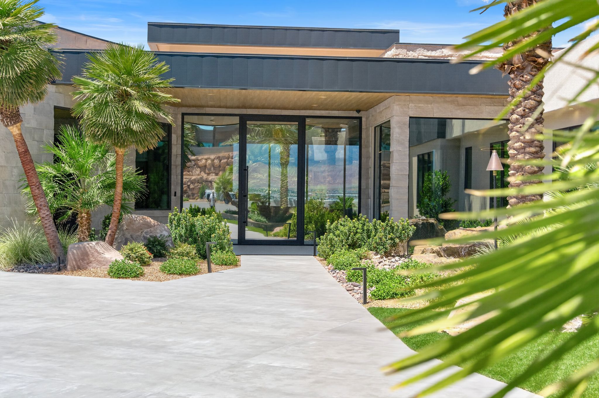 Modern architectural exterior featuring a stucco and stone facade, flat roofline, and expansive glass entry doors
