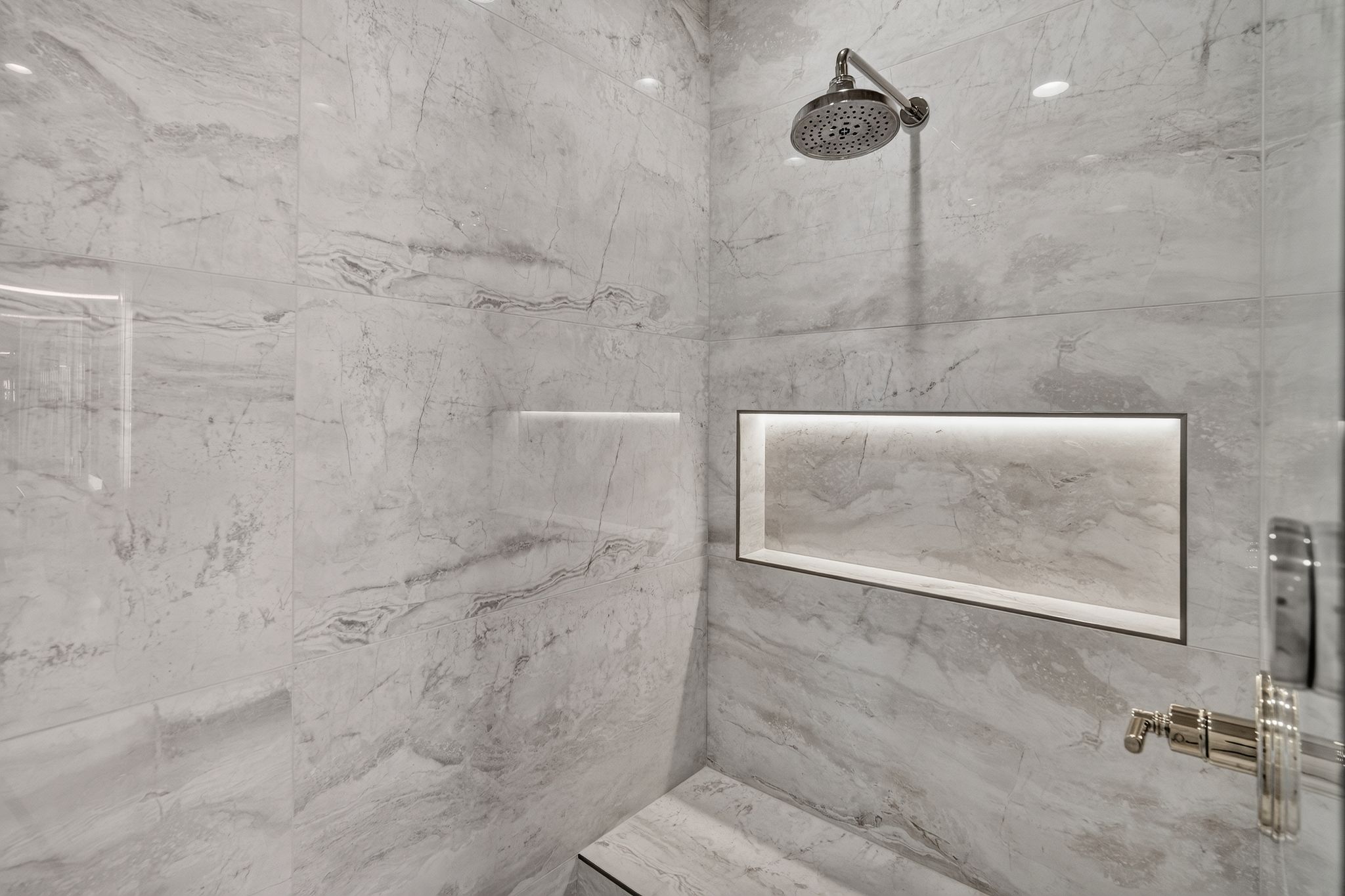 Shower featuring large format marble-look tile, a built-in bench, a recessed niche with integrated lighting, a rainfall showerhead, and polished nickel fixtures