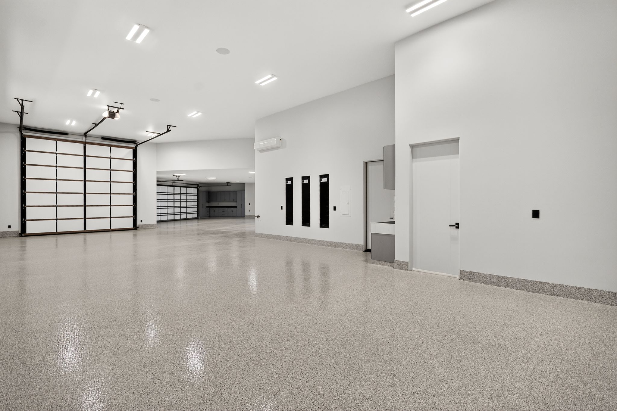 Spacious garage featuring a durable epoxy floor, multiple overhead sectional doors with translucent panels, and extensive overhead lighting