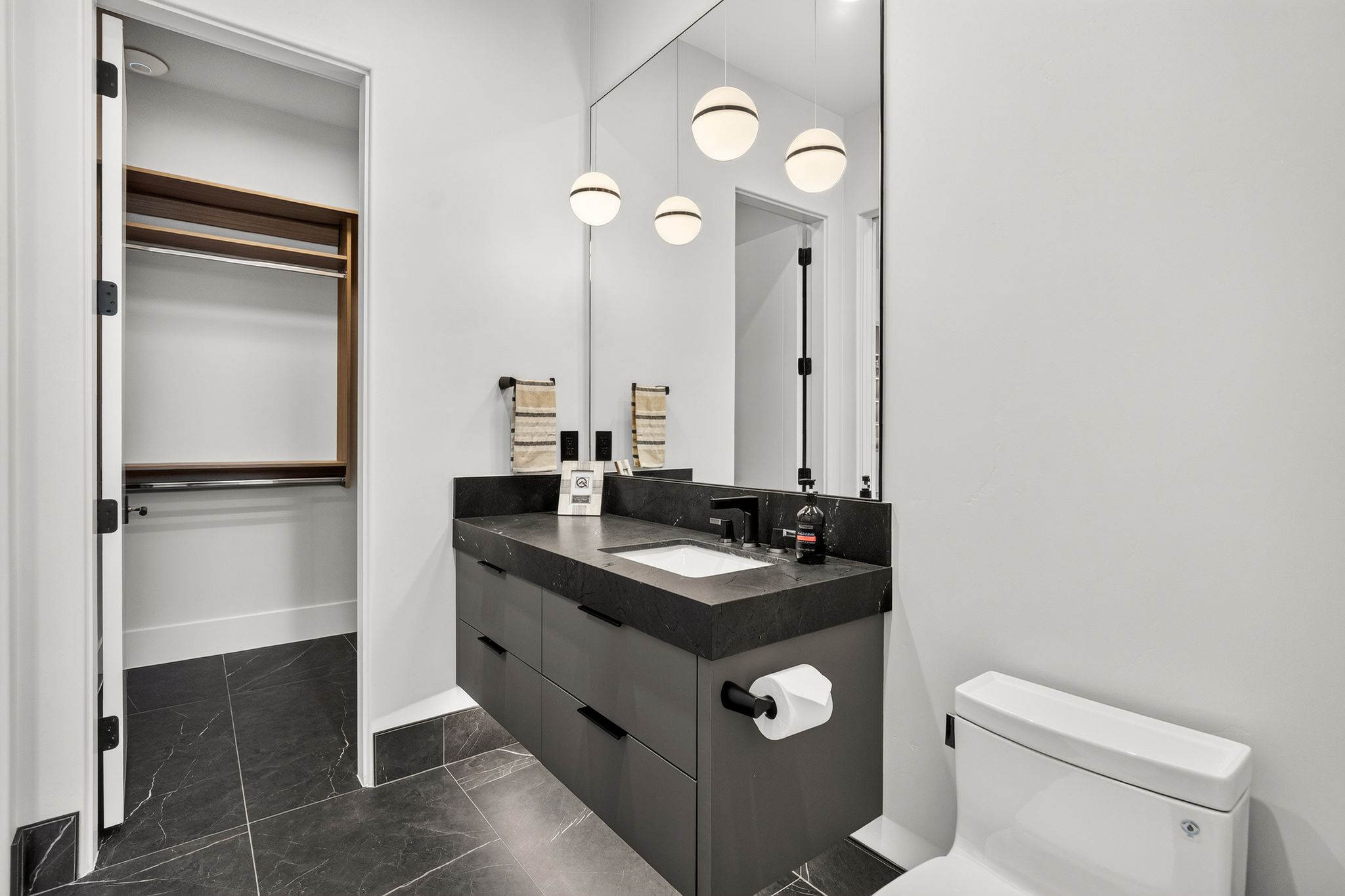 Bathroom vanity with a dark countertop and integrated sink, under-mount cabinetry, and a full-height mirror