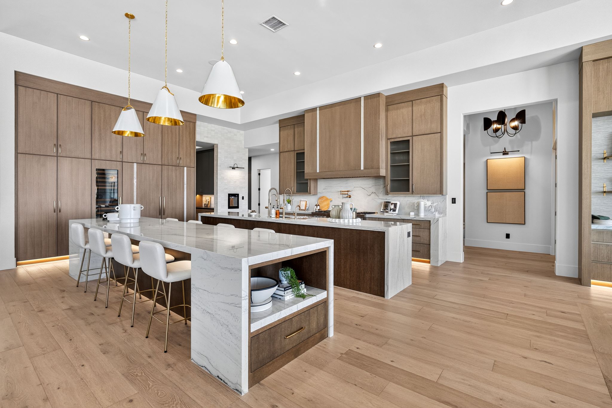 Expansive kitchen featuring light wood-finish flooring, two large kitchen islands with stone countertops, and extensive built-in cabinetry