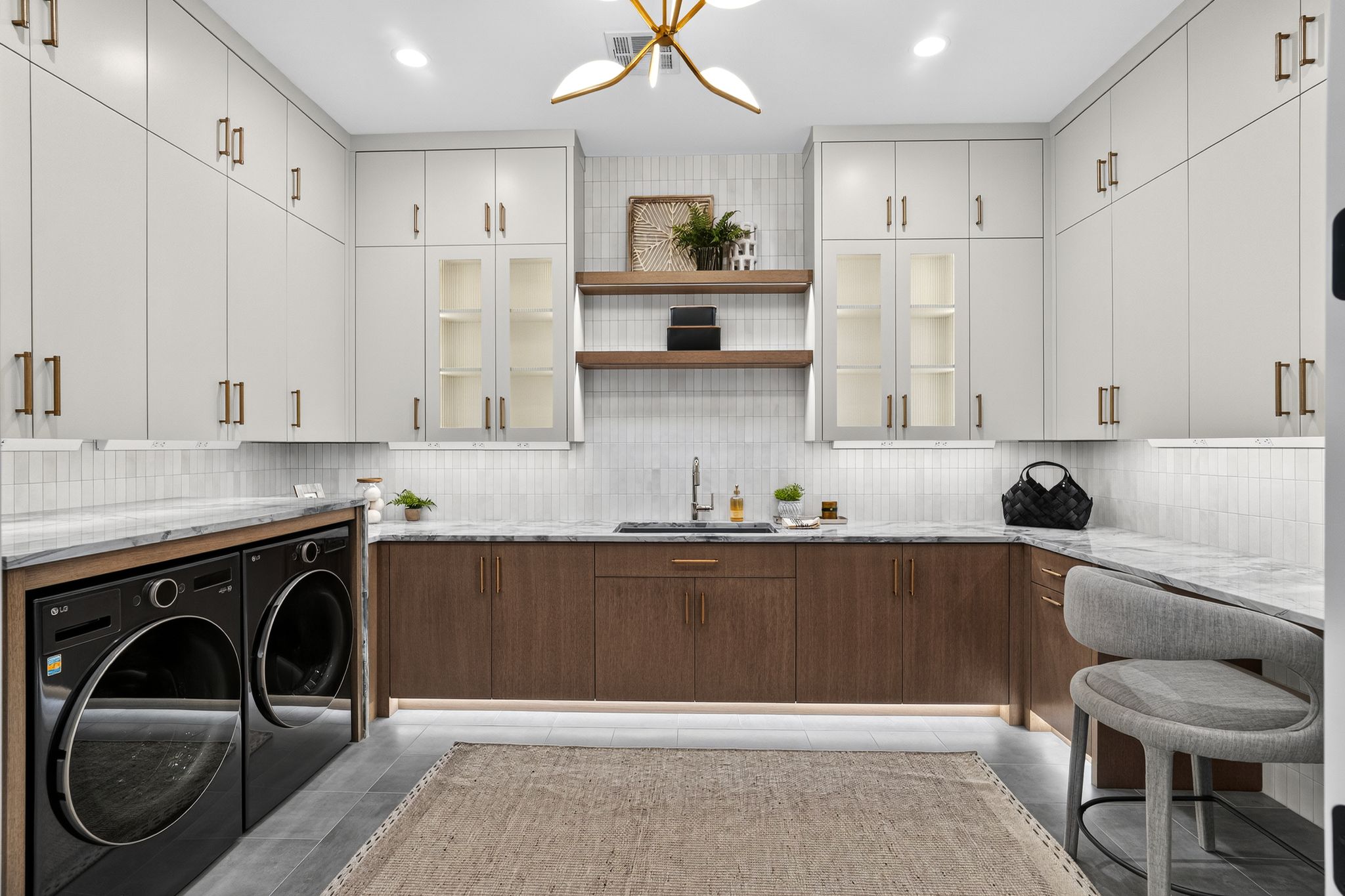 Laundry room featuring extensive upper and lower cabinetry, integrated washer and dryer units, a utility sink, and stone countertops