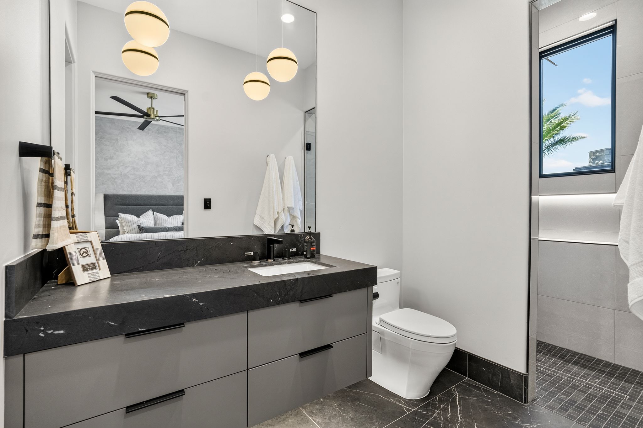 Modern bathroom with a dark stone countertop vanity, an integrated rectangular sink, a wall-mounted mirror, and contemporary spherical pendant lighting