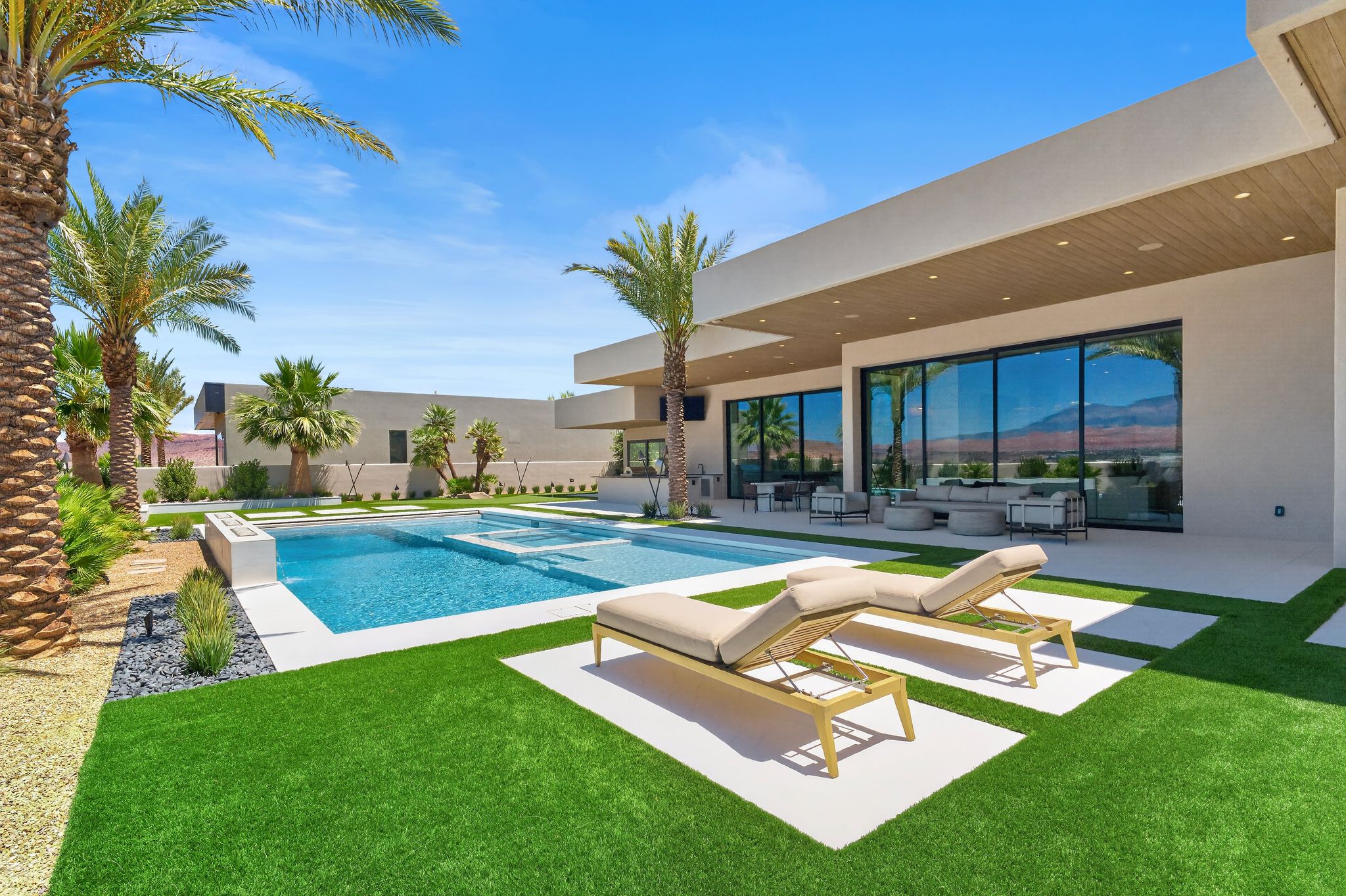 Expansive outdoor space featuring a rectangular swimming pool with integrated spa, surrounded by artificial turf and large format paver stones