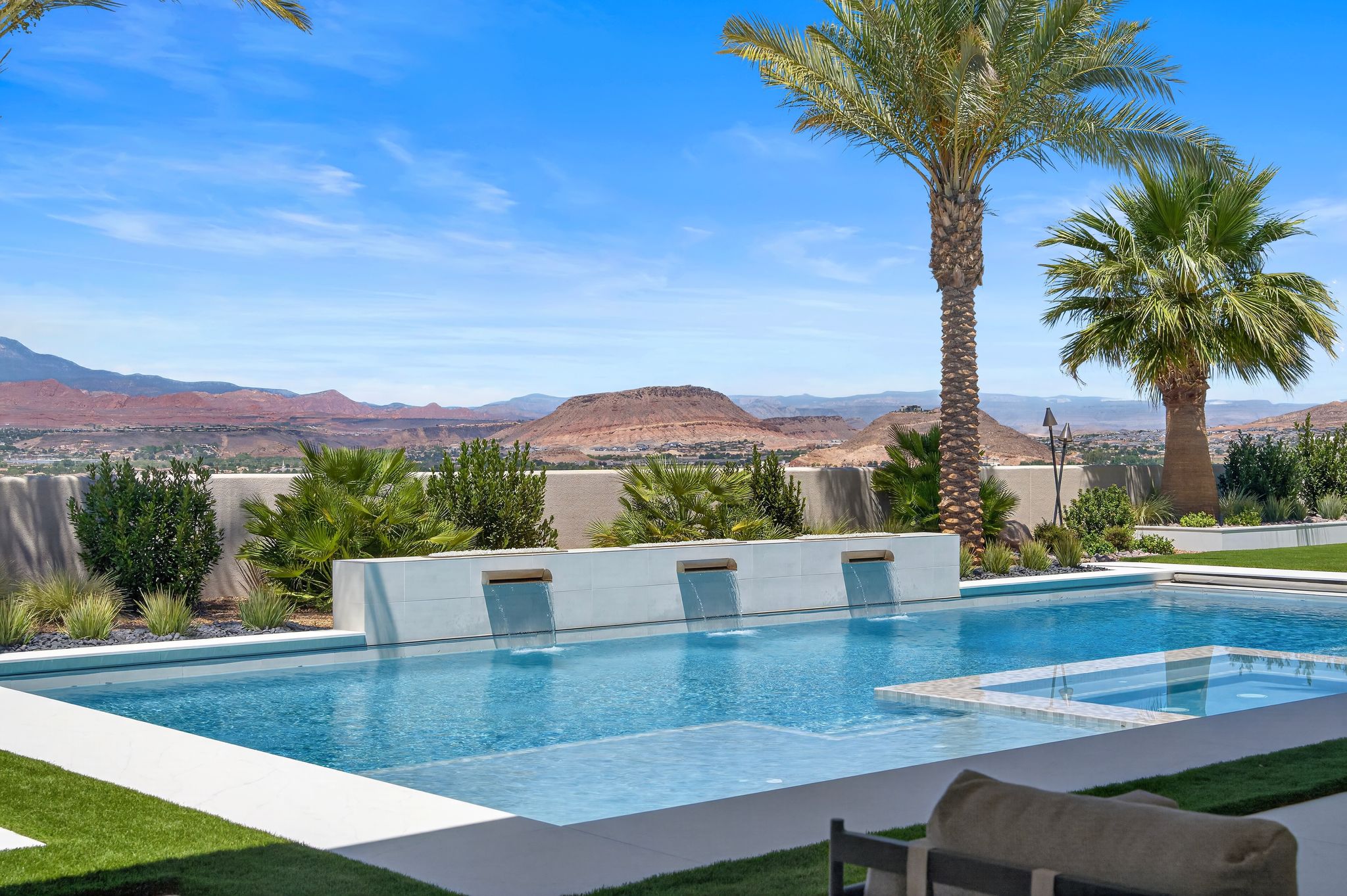 Outdoor entertaining area featuring a rectangular pool with integrated spa, multiple water features, and a surrounding artificial turf patio