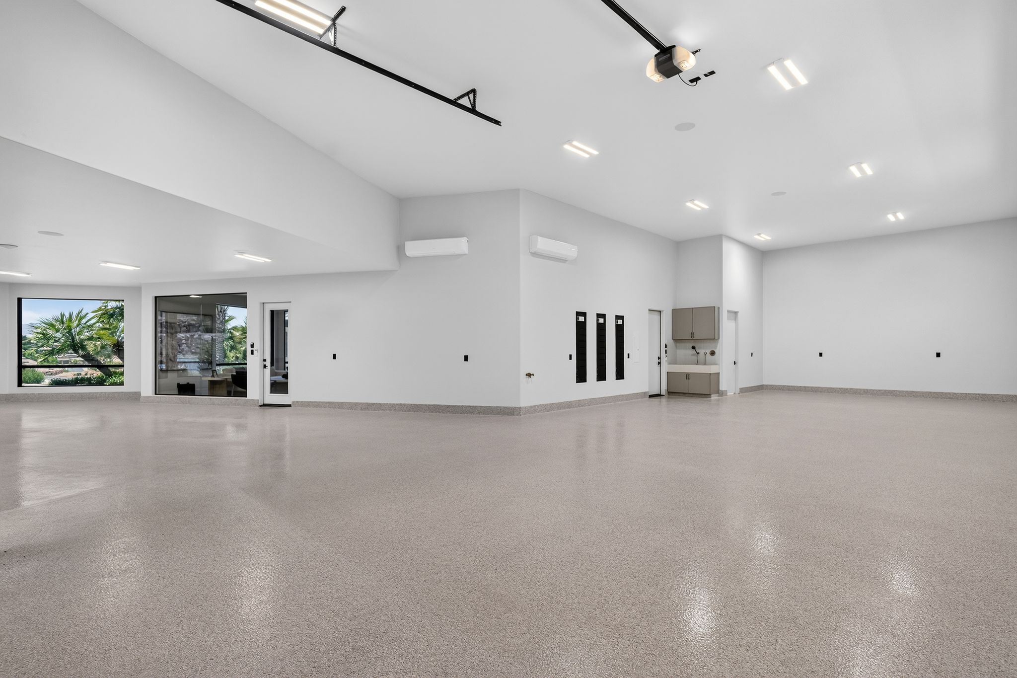 Spacious garage featuring high ceilings, epoxy flooring, large windows, recessed lighting, and built-in cabinetry with a utility sink