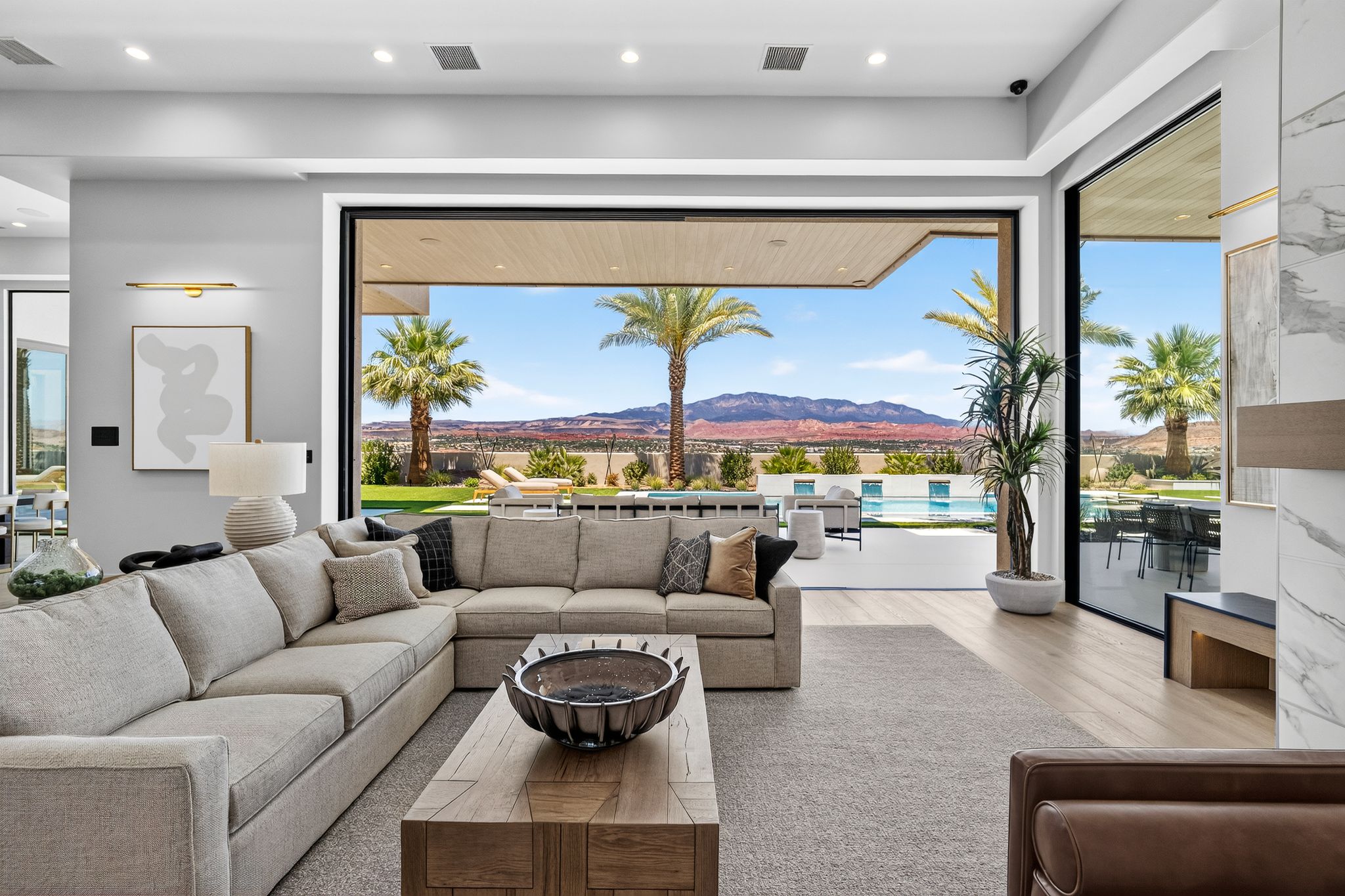 Spacious living area featuring expansive glass doors, light wood-finish flooring, a contemporary fireplace with a stone-finish facade, and recessed ceiling lighting