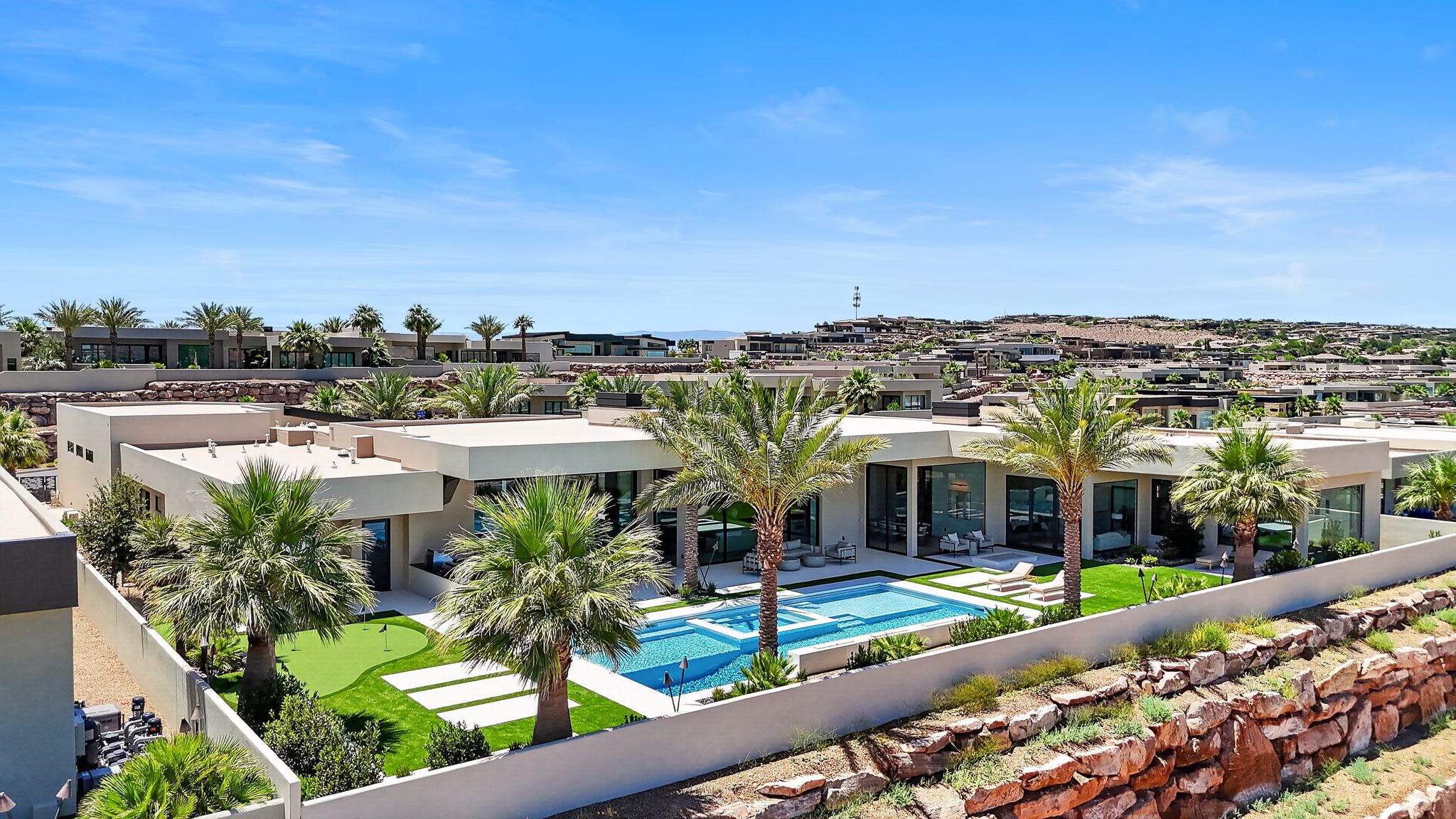 Contemporary desert architecture featuring a private courtyard, expansive pool, integrated spa, putting green, and mature palm trees