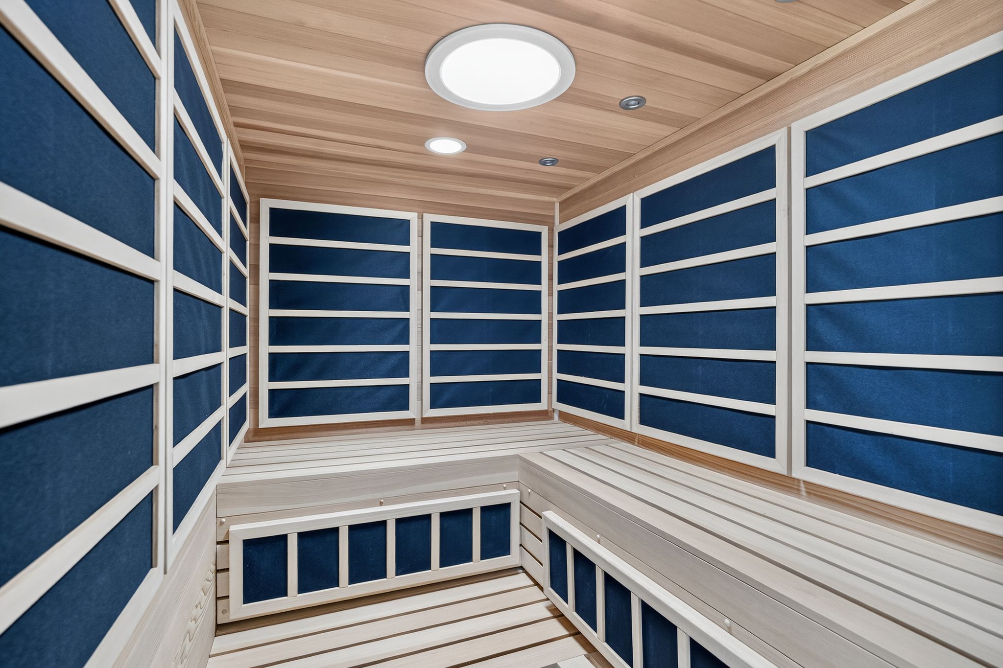 Interior sauna featuring wood paneling, built-in benches, recessed lighting, and a circular overhead light fixture