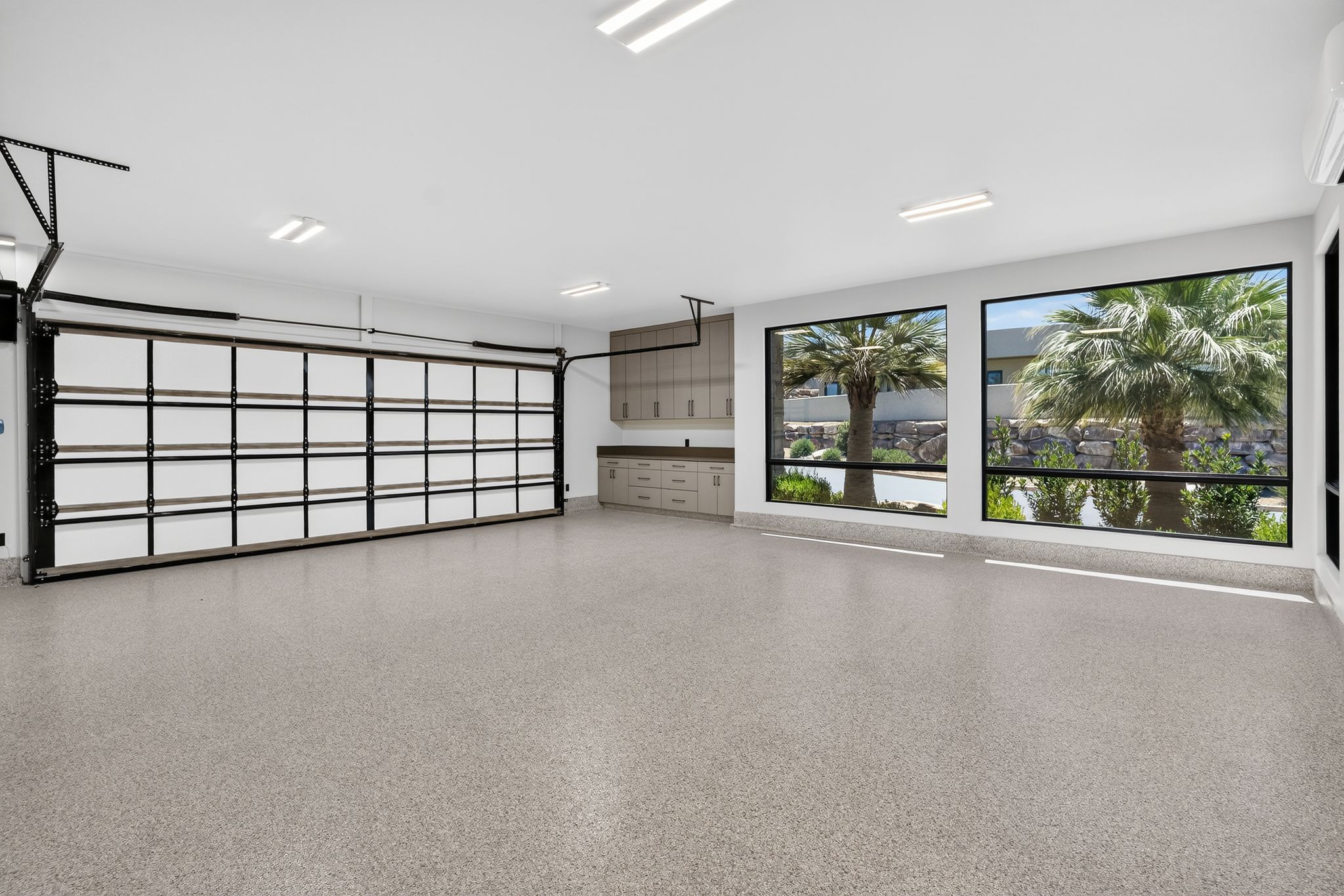 Spacious garage featuring a glass-paneled sectional door, epoxy-coated flooring, and large windows
