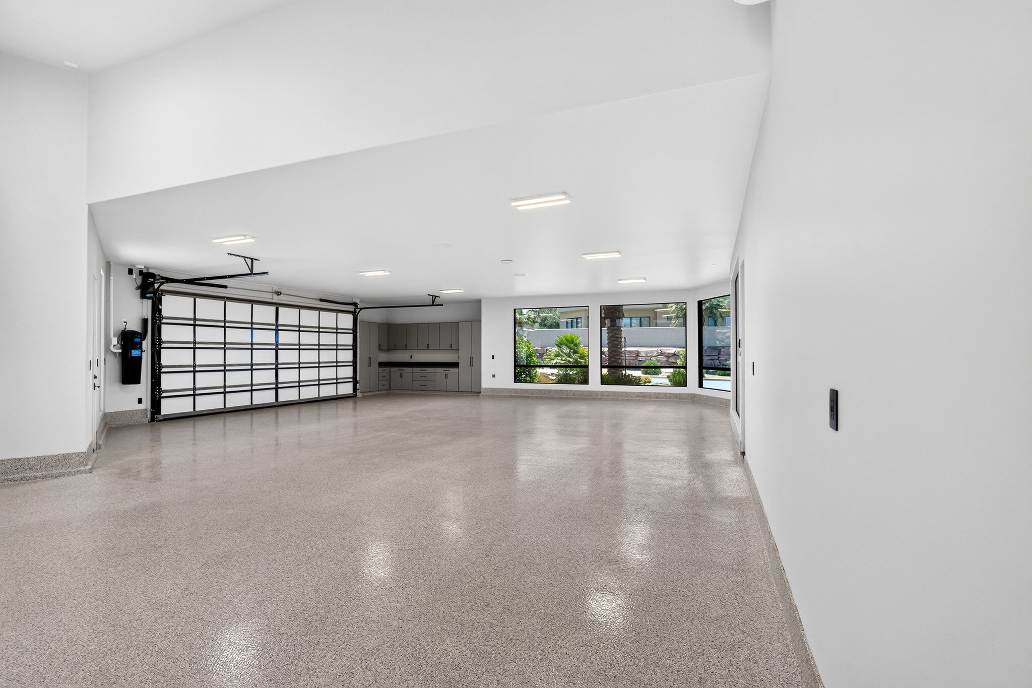 Expansive garage featuring a glass panel garage door, polished concrete flooring, built-in cabinetry, and multiple windows