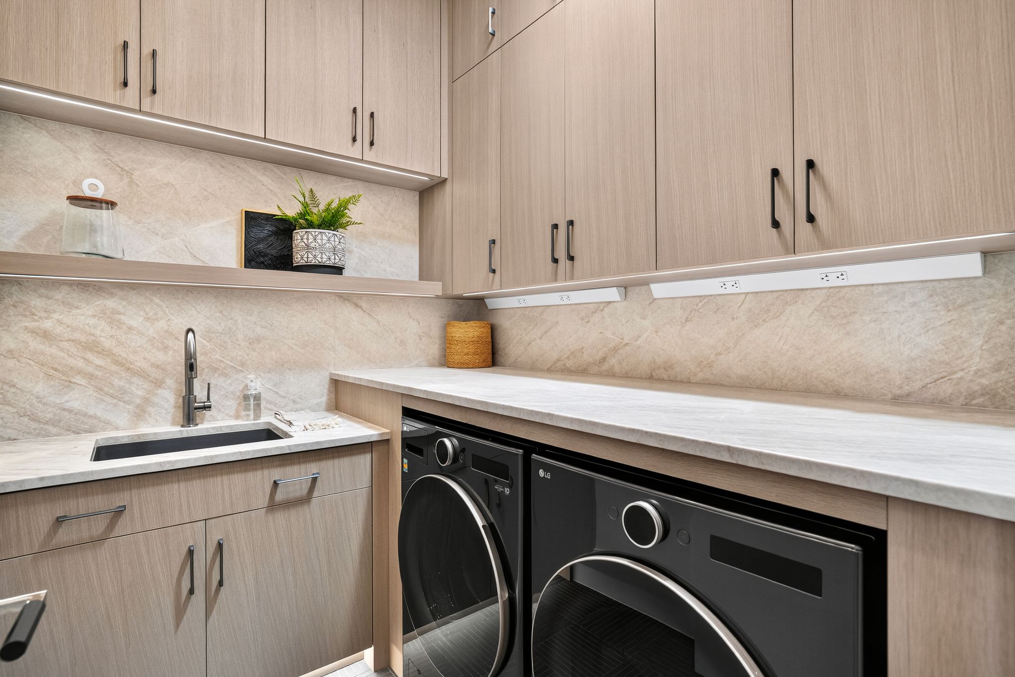 Integrated laundry area featuring light wood-finish cabinetry, a stone-finish backsplash, and light stone-finish countertops