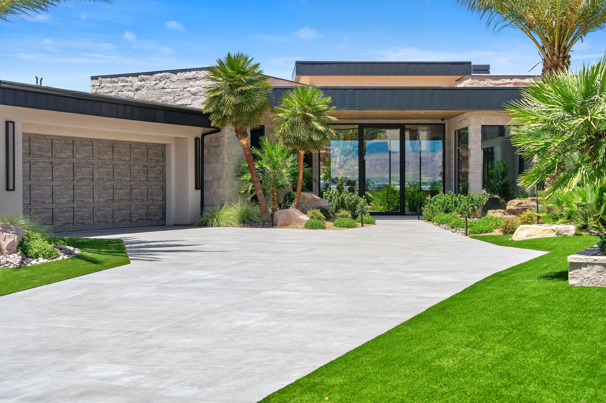 Contemporary exterior featuring a stone facade, a multi-panel garage door, a prominent glass entry, and a concrete driveway