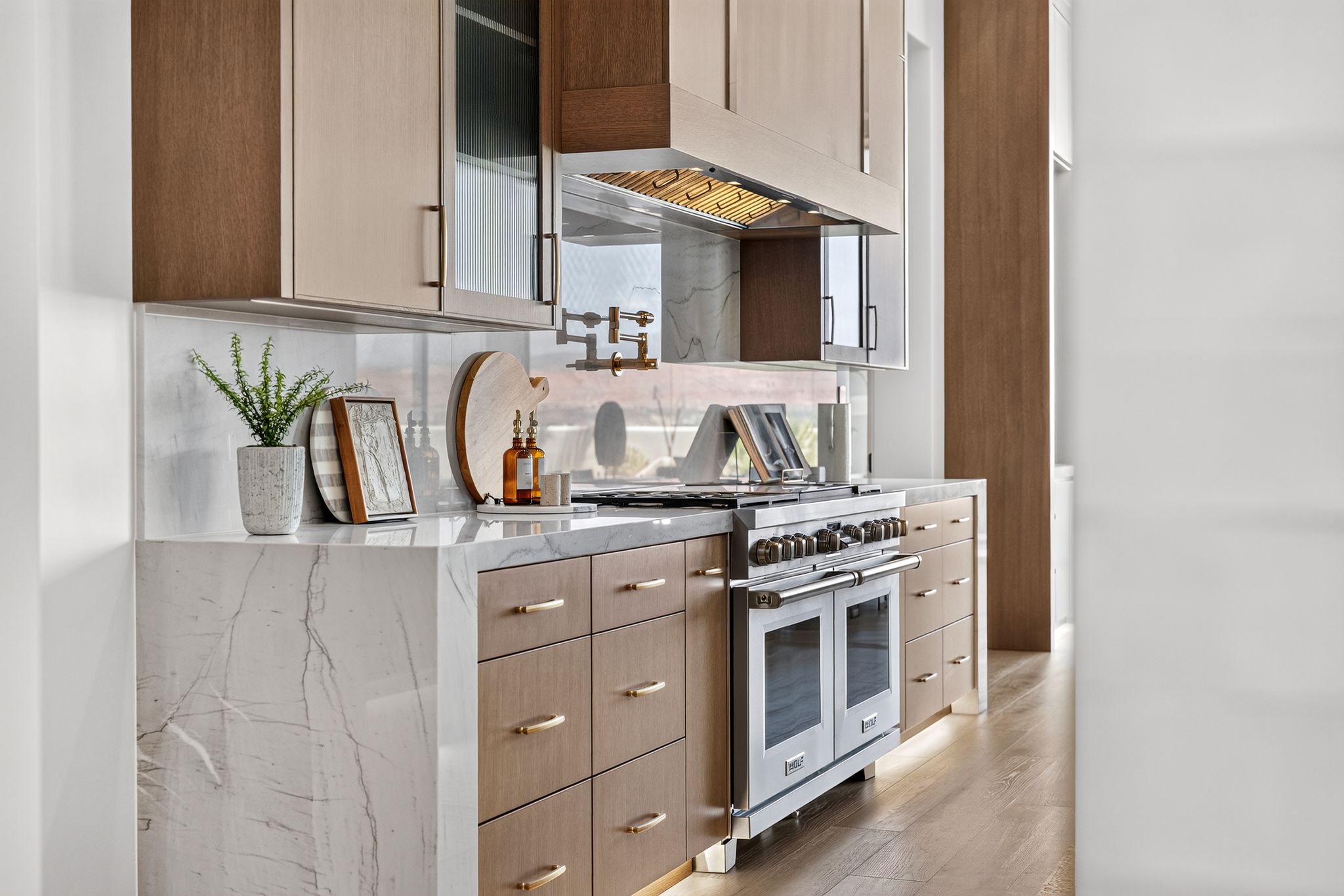Gourmet kitchen featuring a stainless steel professional range, a pot filler faucet, stone countertops with waterfall edge, and custom cabinetry with varied finishes