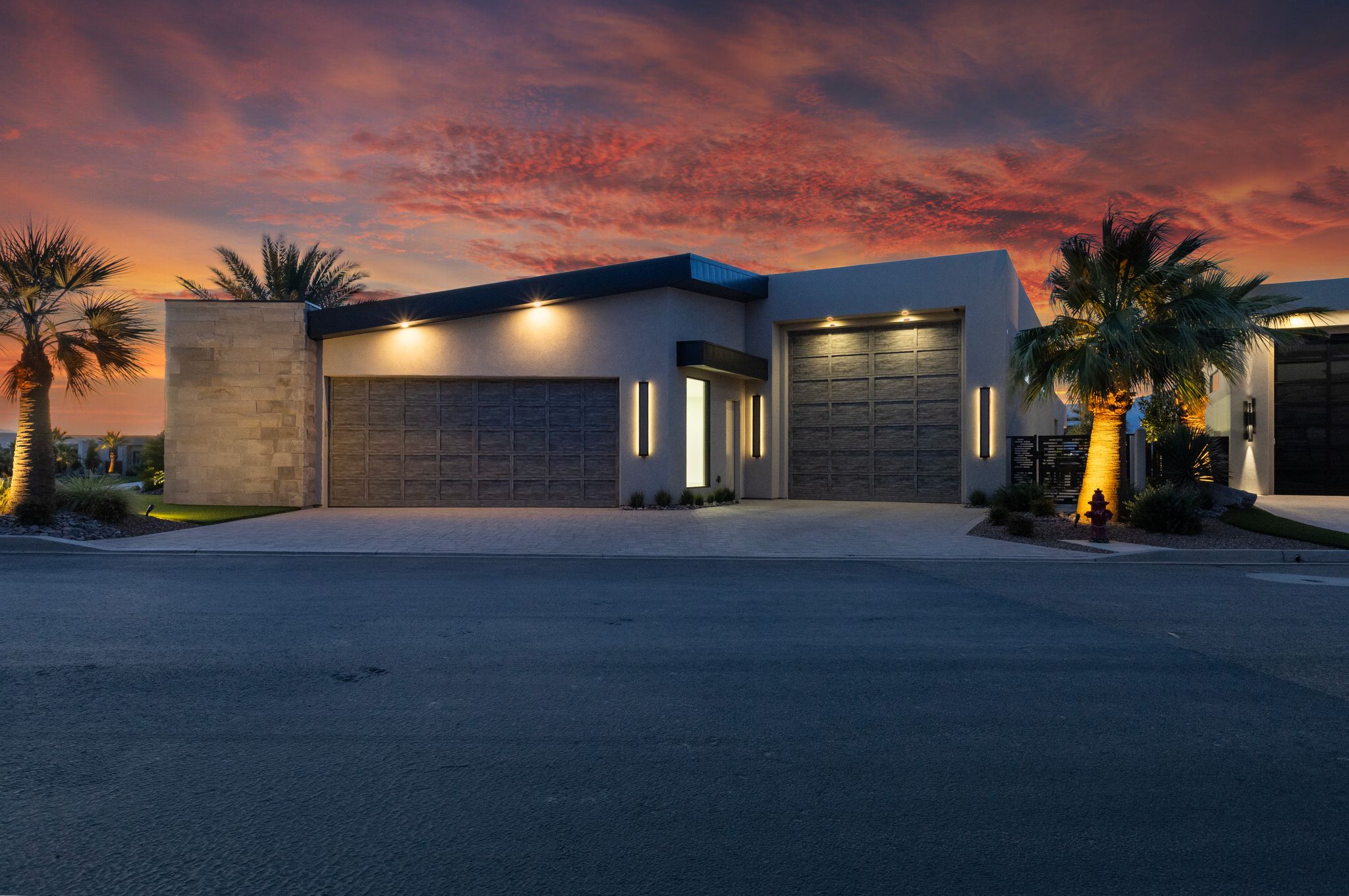 Contemporary residence featuring a stucco and stone exterior, two garage doors with textured panels, and integrated exterior lighting
