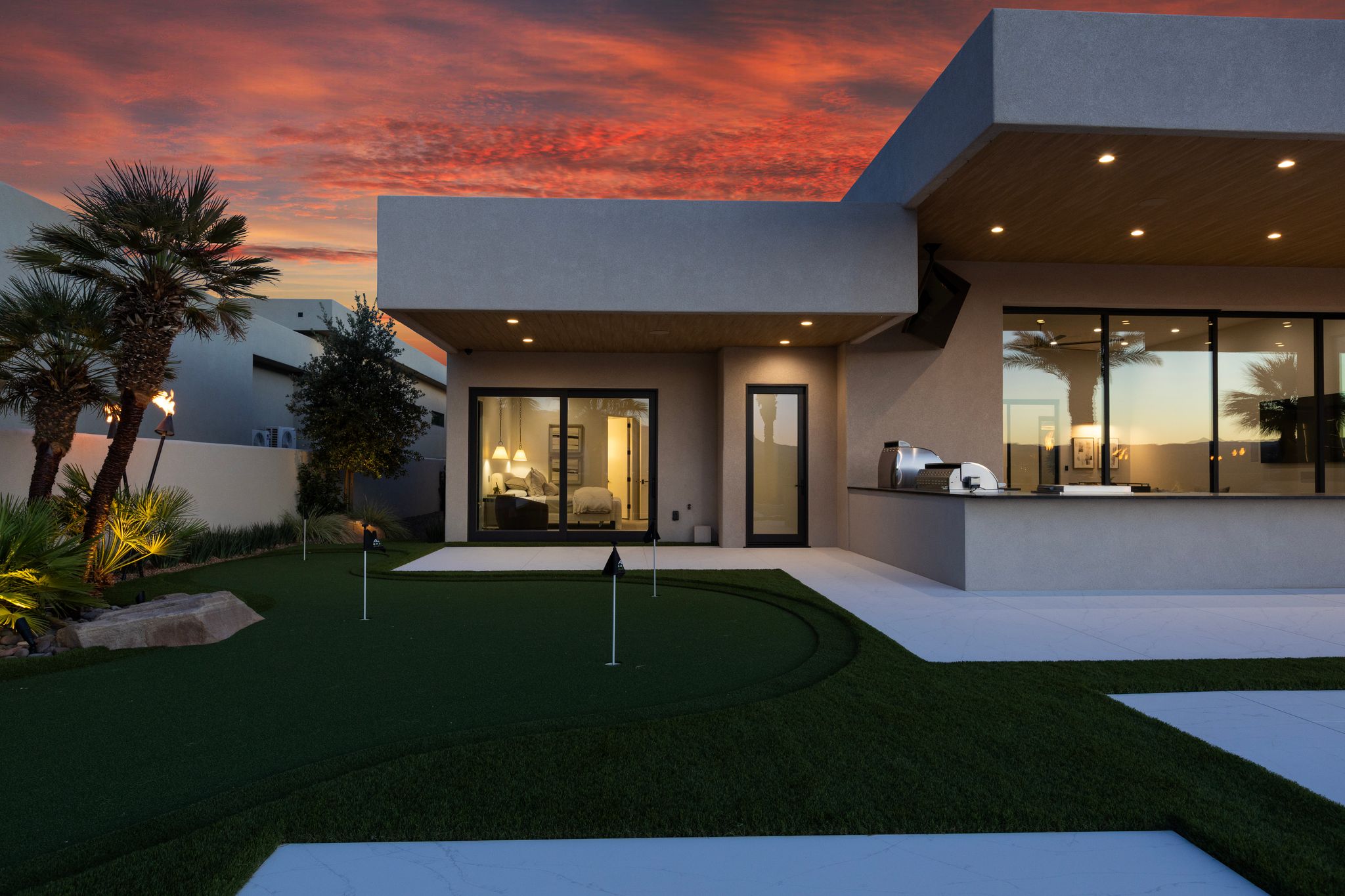 Outdoor entertainment space featuring a built-in putting green, integrated outdoor kitchen with a grill, expansive sliding glass doors, contemporary exterior lighting, and accent landscaping