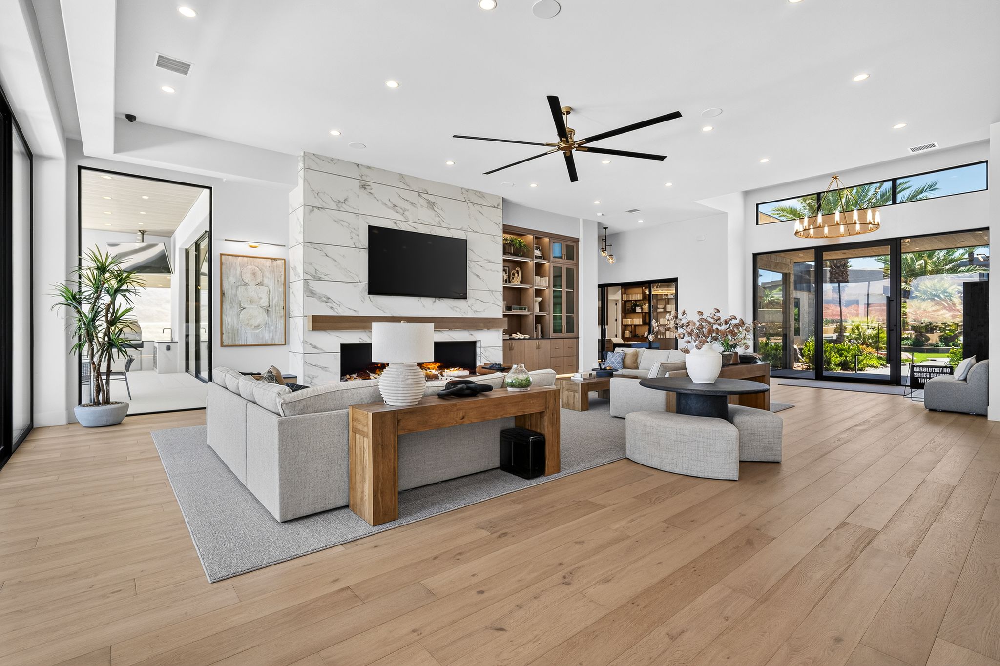 Spacious living area featuring light wood-finish flooring, a large marble-clad fireplace with a wood mantle, and extensive recessed lighting