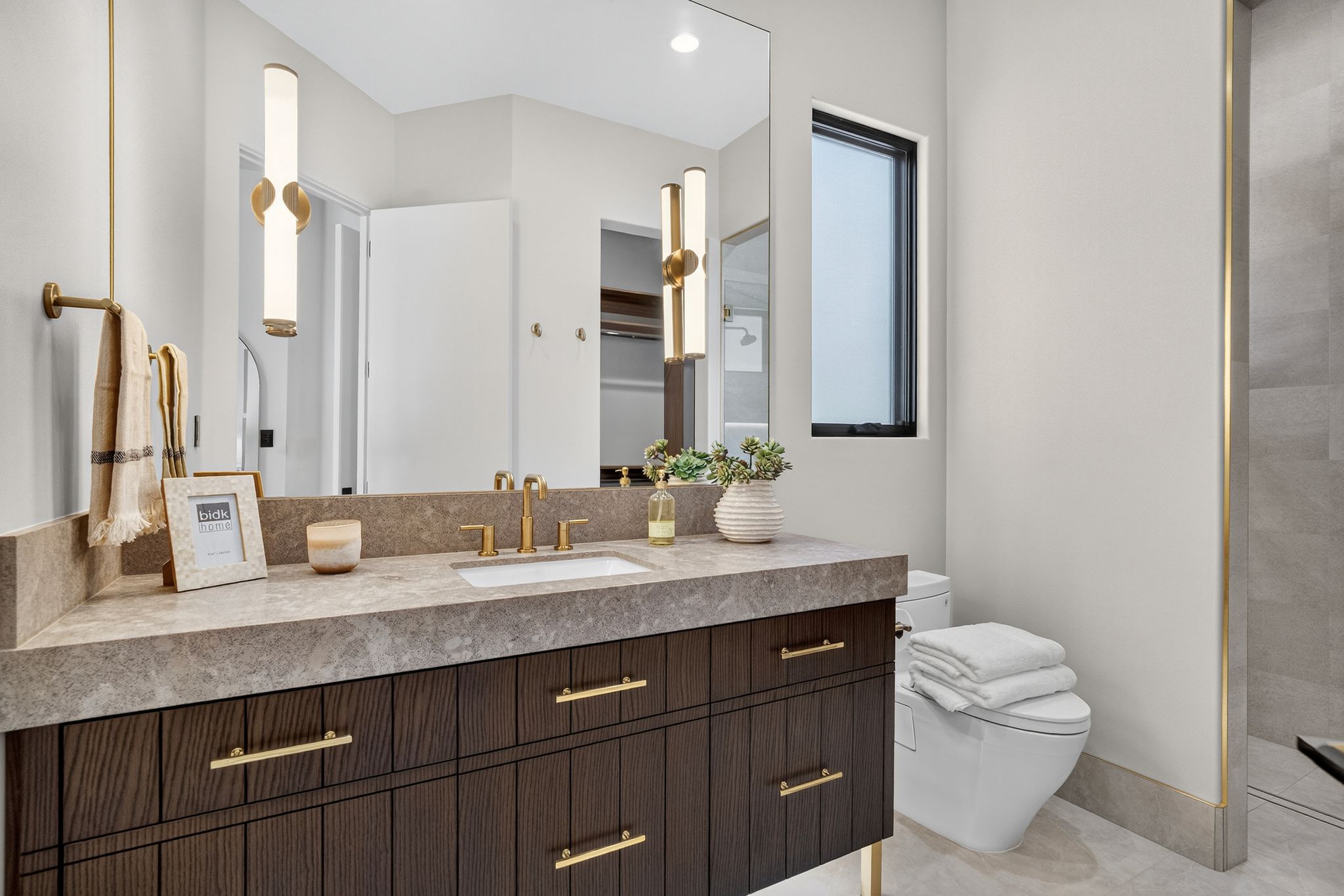 Dark wood vanity with gold-tone hardware, rectangular undermount sink, and a stone-finish countertop