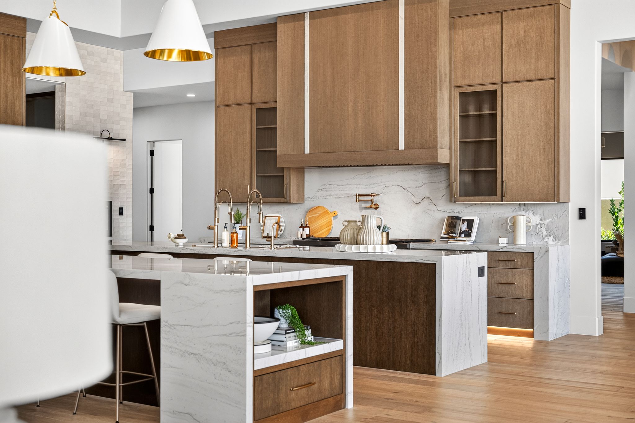 Gourmet kitchen featuring a waterfall island, wood-finish cabinetry, integrated appliances, and a full-height stone backsplash