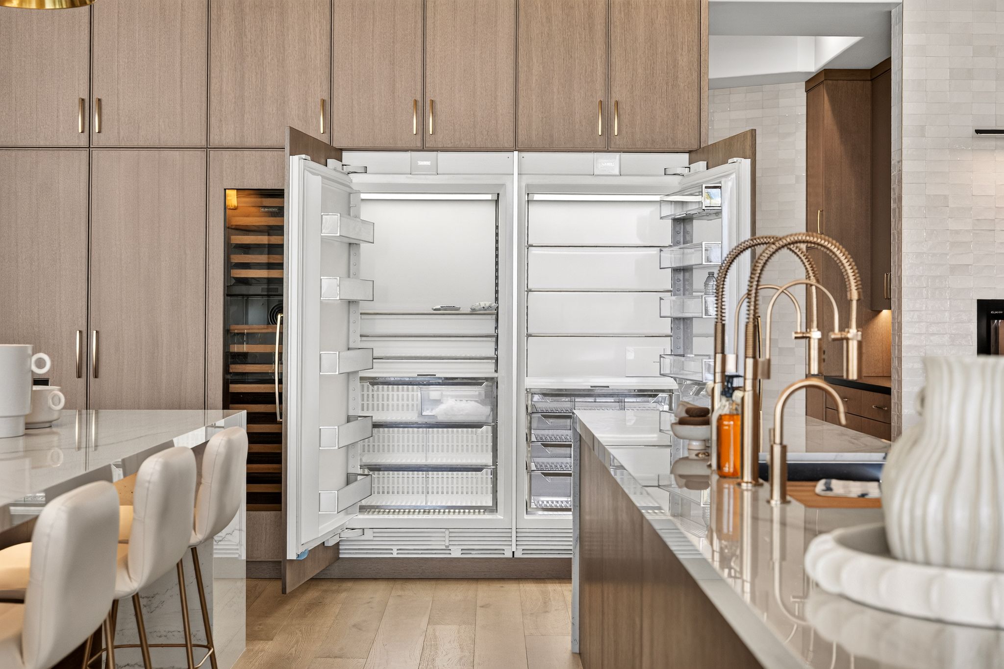 Integrated double-door refrigerator with a built-in wine cooler, complemented by light wood-finish cabinetry and light-toned wood-finish flooring
