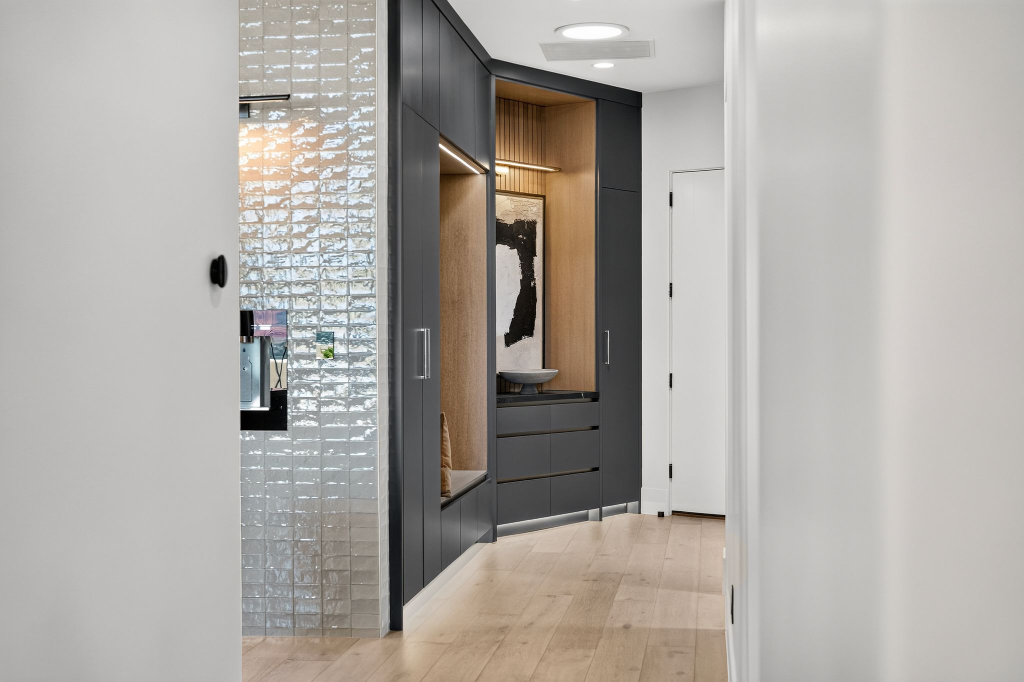 Hallway featuring wood-finish flooring, recessed lighting, and a built-in cabinetry system with dark flat-panel doors and light wood-paneled interior accents