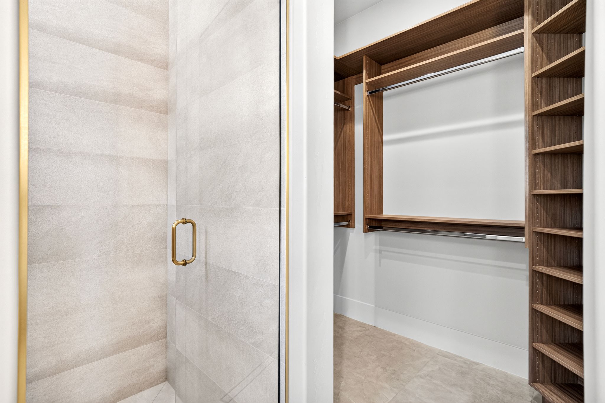 Glass shower enclosure with brass-finish framing and handle, alongside a walk-in closet featuring wood-finish shelving and hanging rods