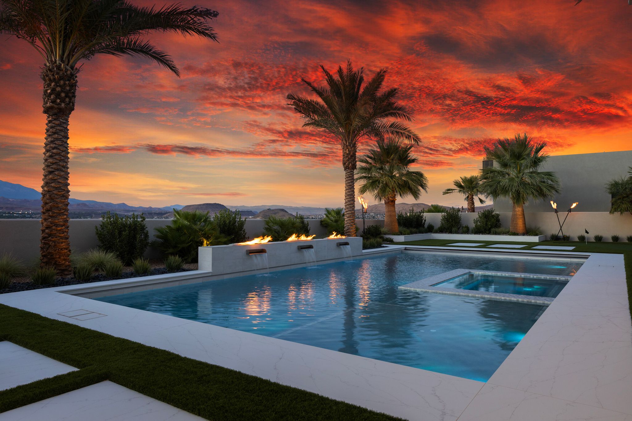 Modern outdoor space featuring a swimming pool with an integrated spa, fire elements, and surrounding artificial turf