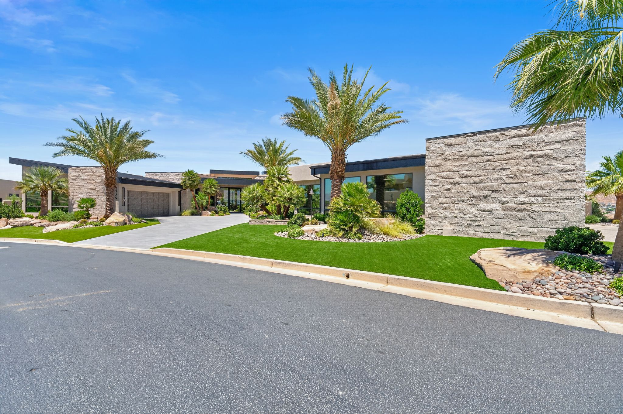 Modern exterior featuring stone accents, a concrete driveway, a two-car garage, and desert-inspired landscaping with artificial turf