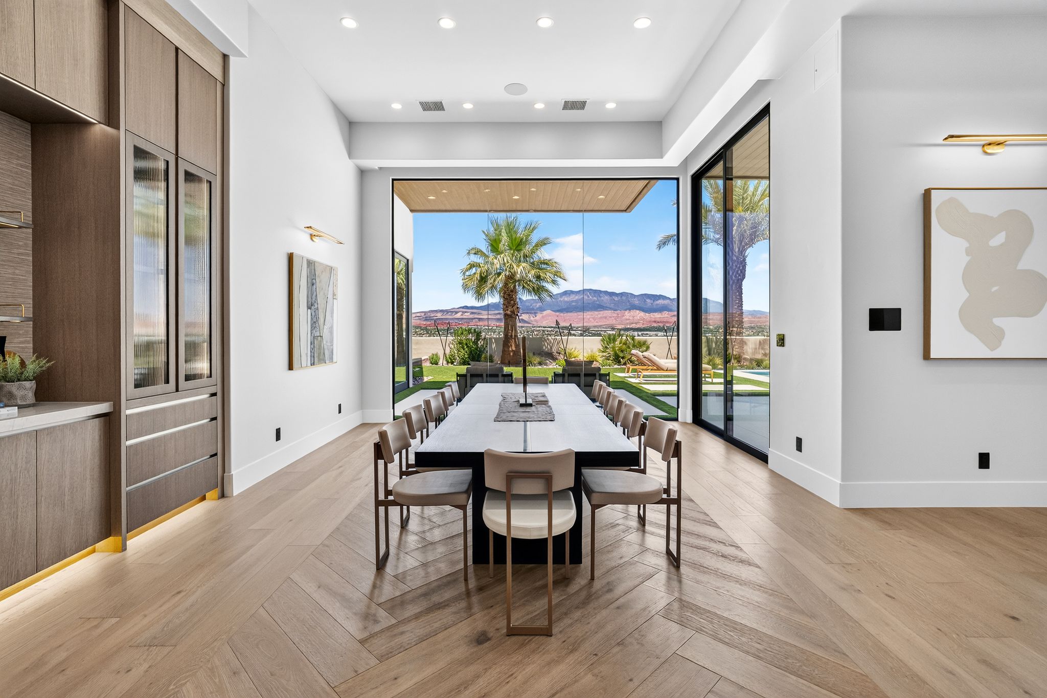 Open-concept interior featuring herringbone wood-finish flooring, built-in cabinetry with glass-front uppers and integrated lighting, and floor-to-ceiling sliding glass doors