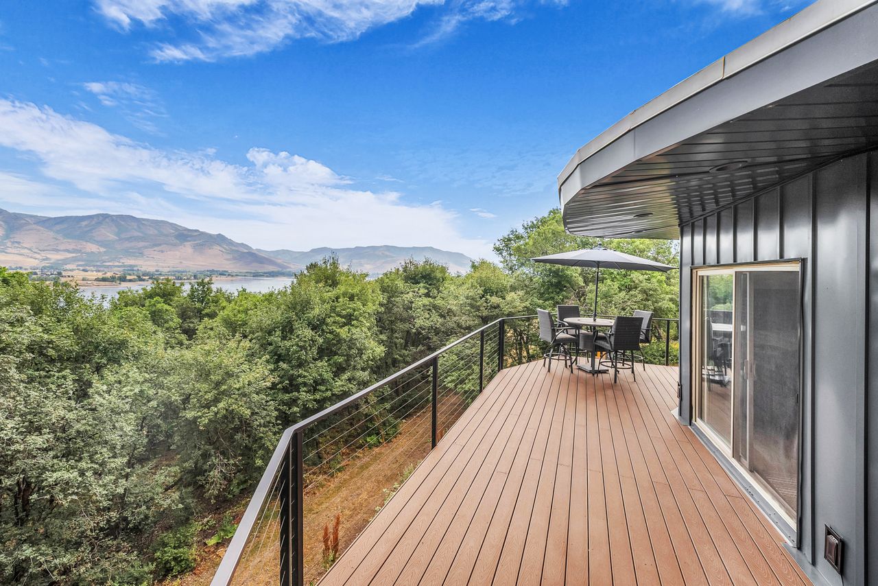 Spacious outdoor deck featuring wide plank wood-finish flooring, a contemporary cable railing system, and a curved architectural design