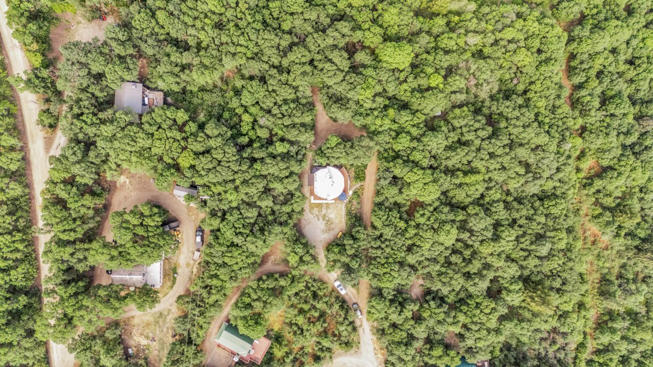 Expansive wooded acreage featuring a central cleared circular pad, multiple structures, and unpaved access roads