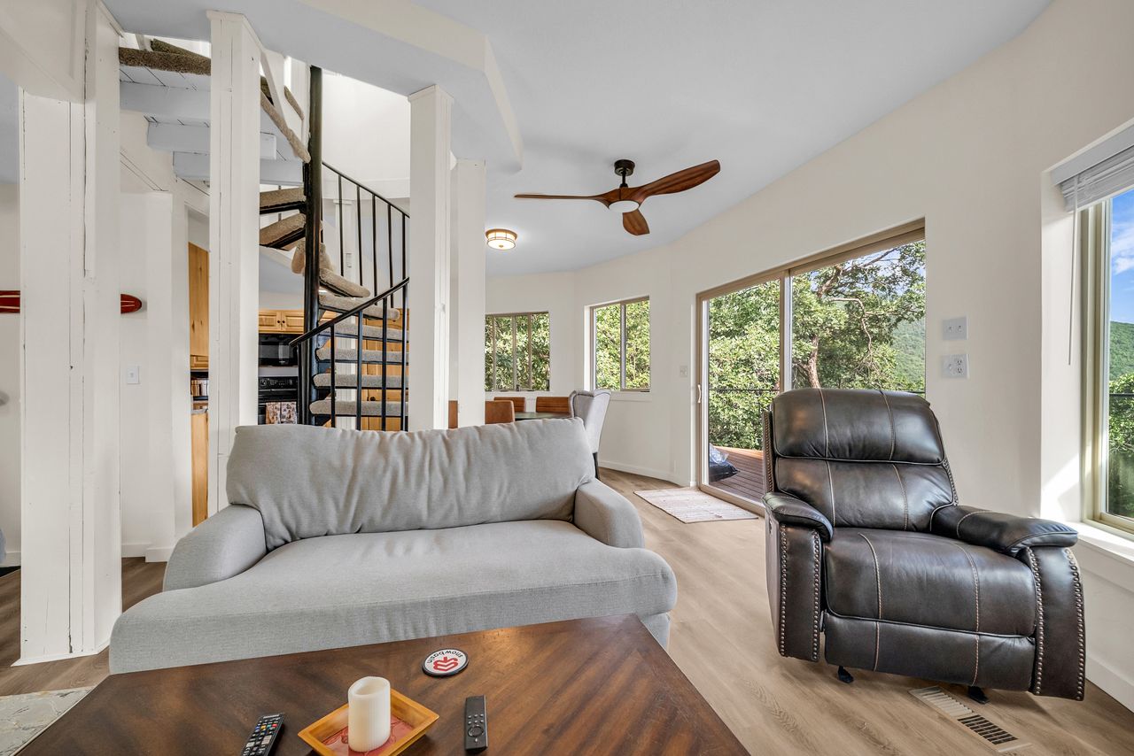 Open-concept living space featuring wood-finish flooring, a contemporary ceiling fan, and a prominent spiral staircase with black metal railing
