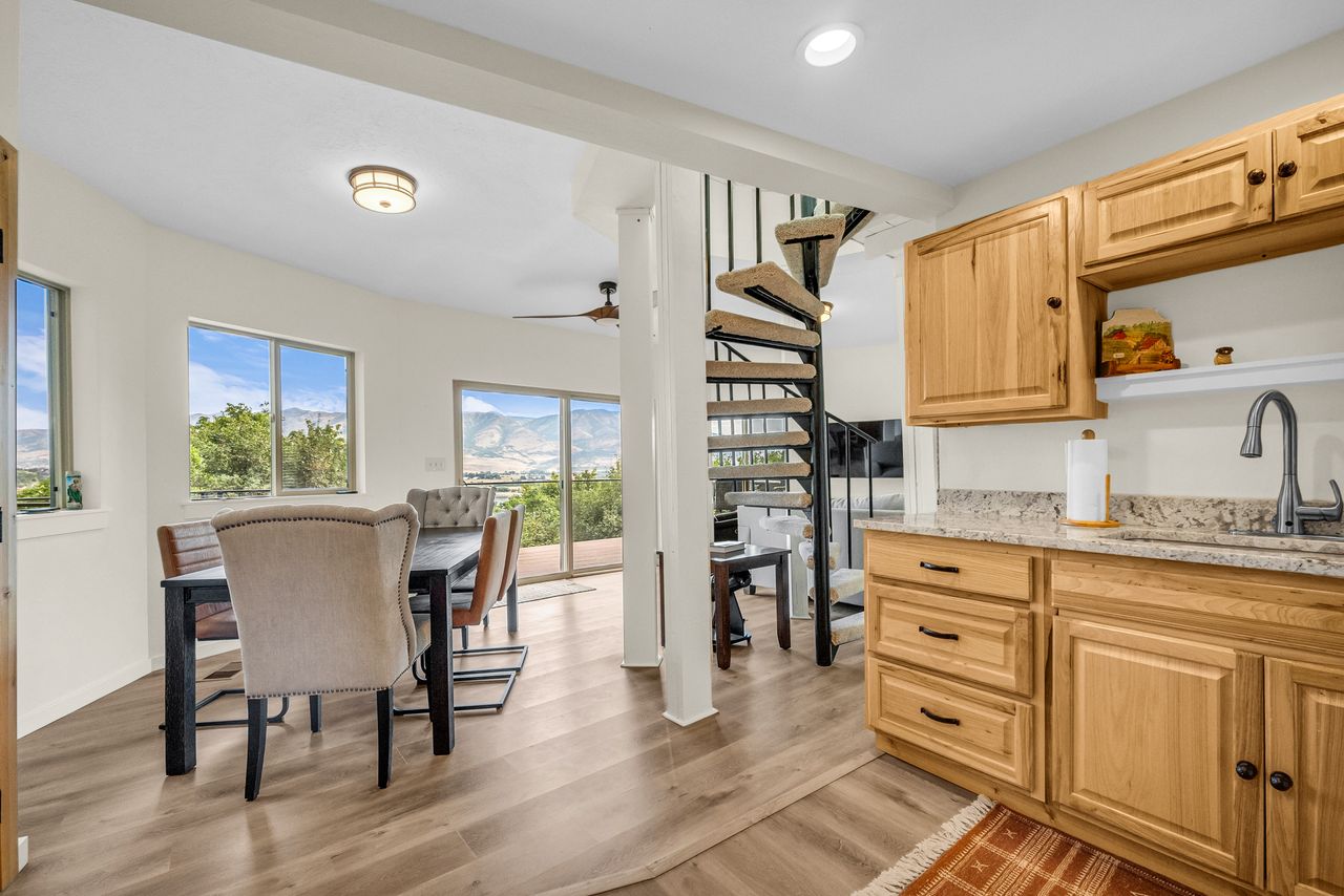 Open-concept living space with wood-finish flooring, a spiral staircase, and light-toned kitchen cabinetry with a light-colored countertop