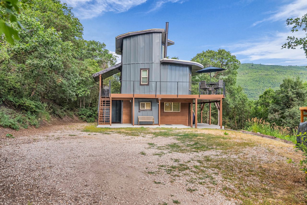 Unique multi-level residence featuring corrugated metal siding, an expansive elevated deck with metal railings, and a lower-level covered patio area