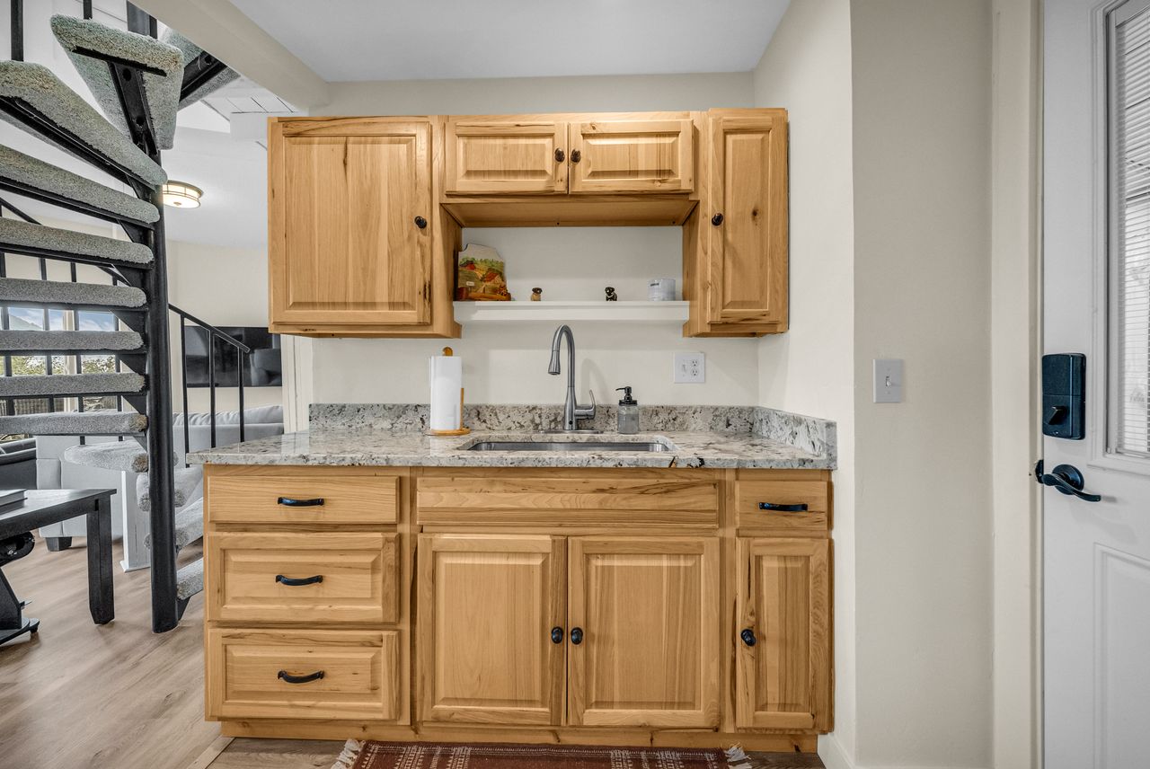 Kitchenette featuring wood cabinetry, stone countertops, and a stainless steel sink with a gooseneck faucet
