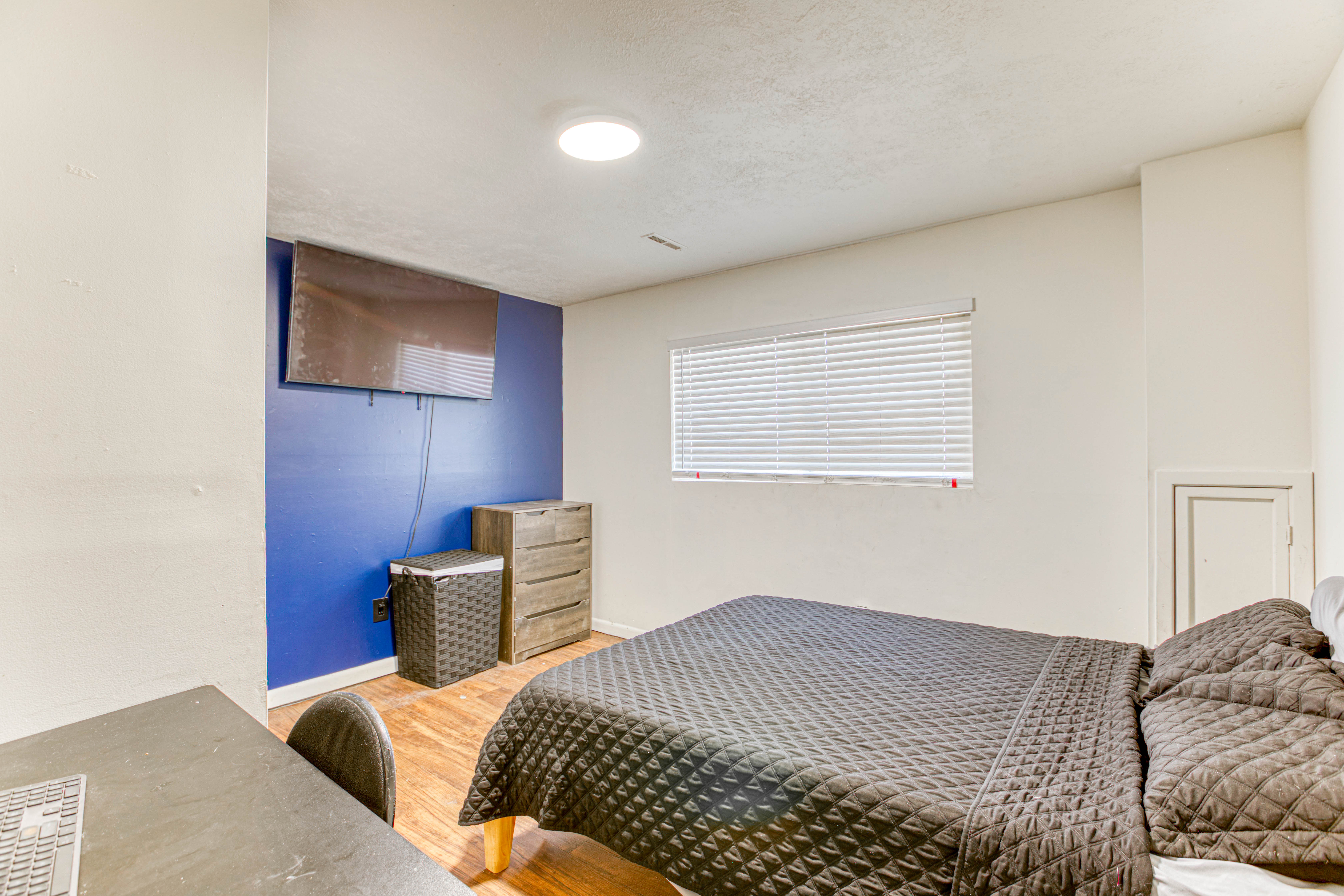Bedroom featuring wood-finish flooring, a wall-mounted television, and a window with blinds