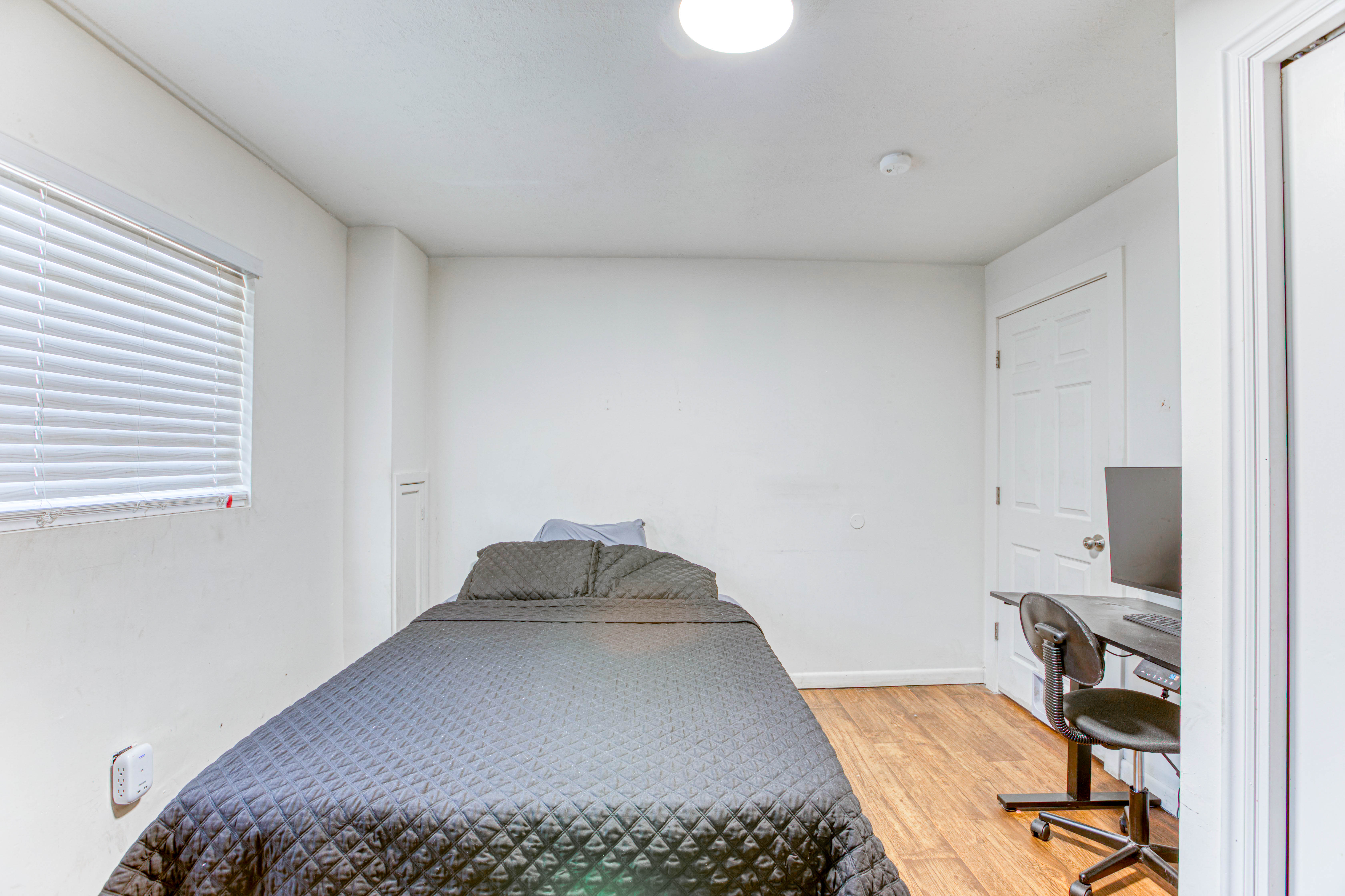 Room with wood-finish flooring, a white paneled door, and a single window with horizontal blinds