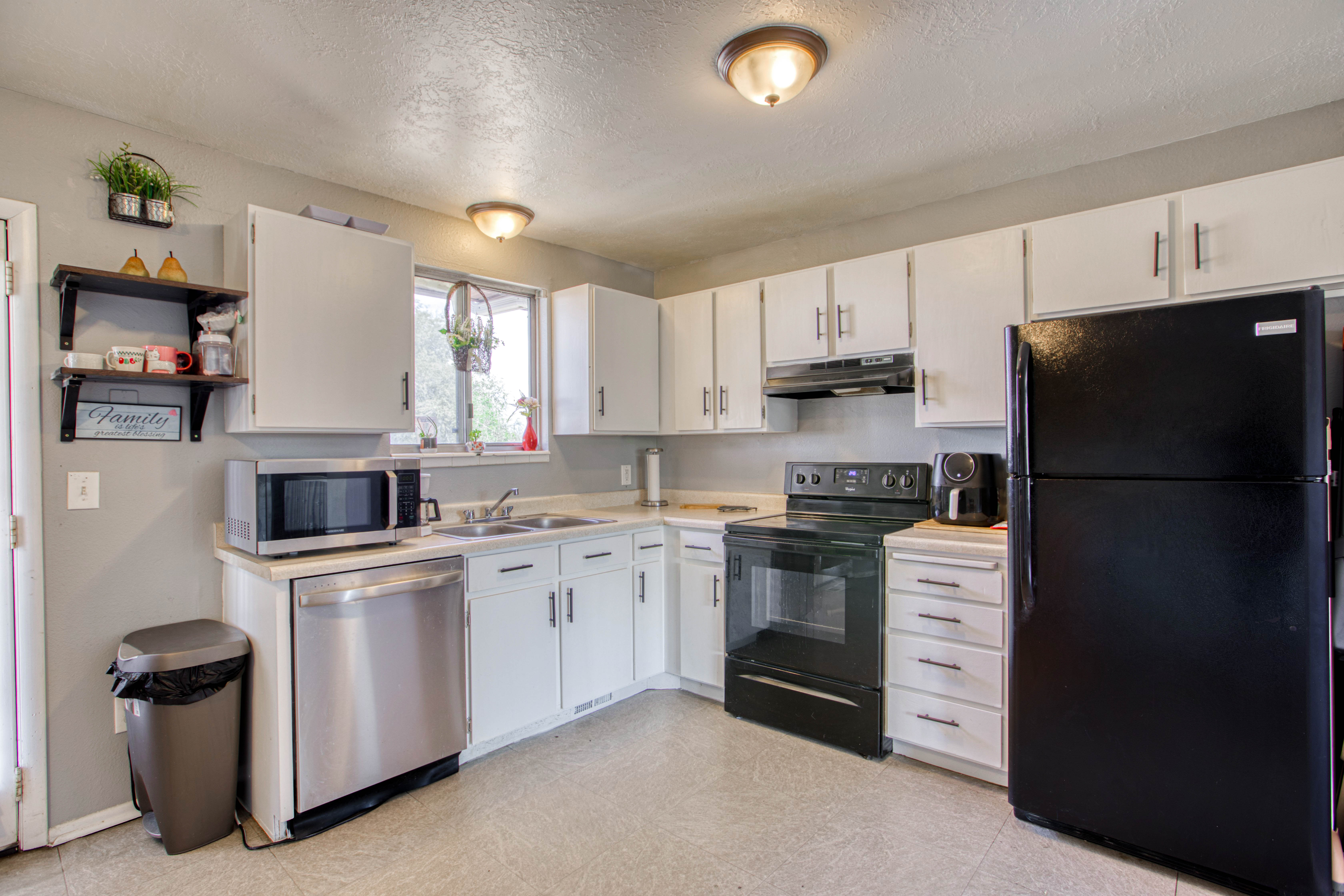 Kitchen featuring white cabinetry, light-toned countertops, a stainless steel dishwasher, a black range with an overhead vent, and a black refrigerator